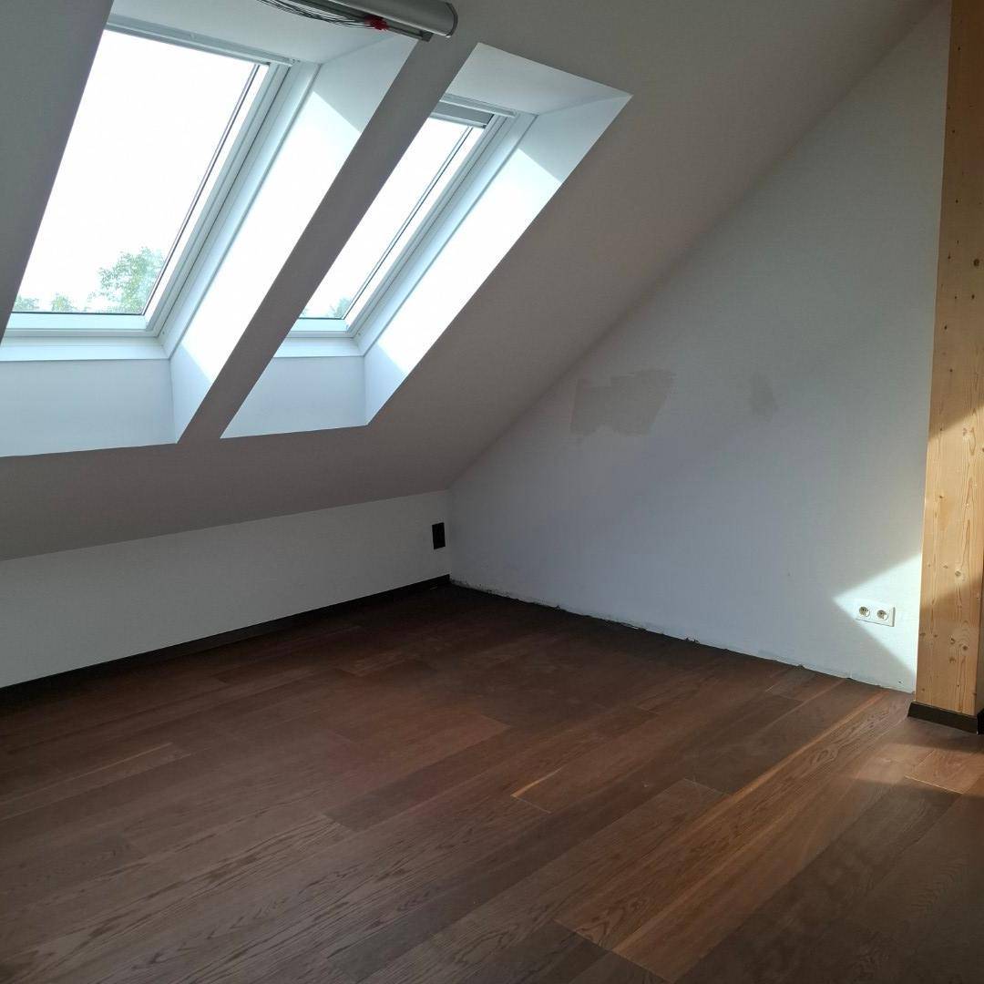 Schlafzimmer mit dunklem Holzboden, weißen Wänden und drei Dachfenstern, die viel Licht spenden.