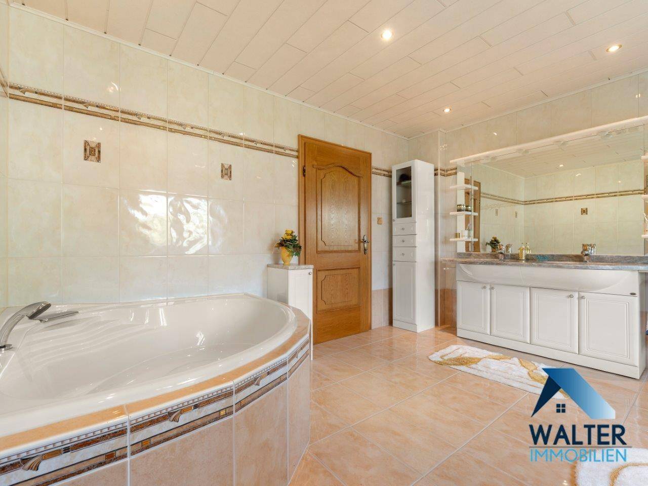 Großes Badezimmer mit Eckbadewanne, Doppelwaschbecken und Spiegelschrank, in warmen Farbtönen gehalten.