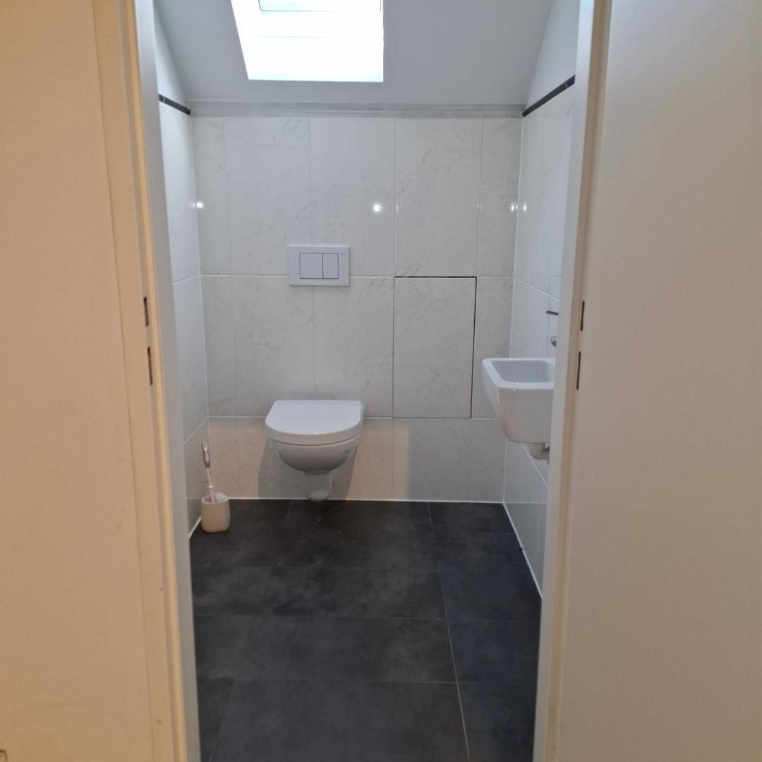 Modernes Gäste-WC mit wandhängendem WC, kleinem Waschbecken und Dachfenster für natürliches Licht.