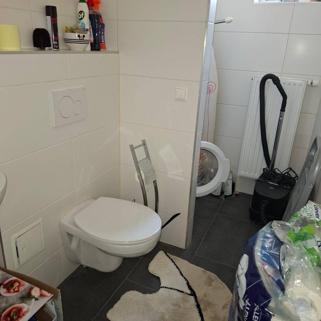 Kleines WC mit Toilette, Waschmaschine und Staubsauger in einem funktionalen Raum, der gut genutzt wird.