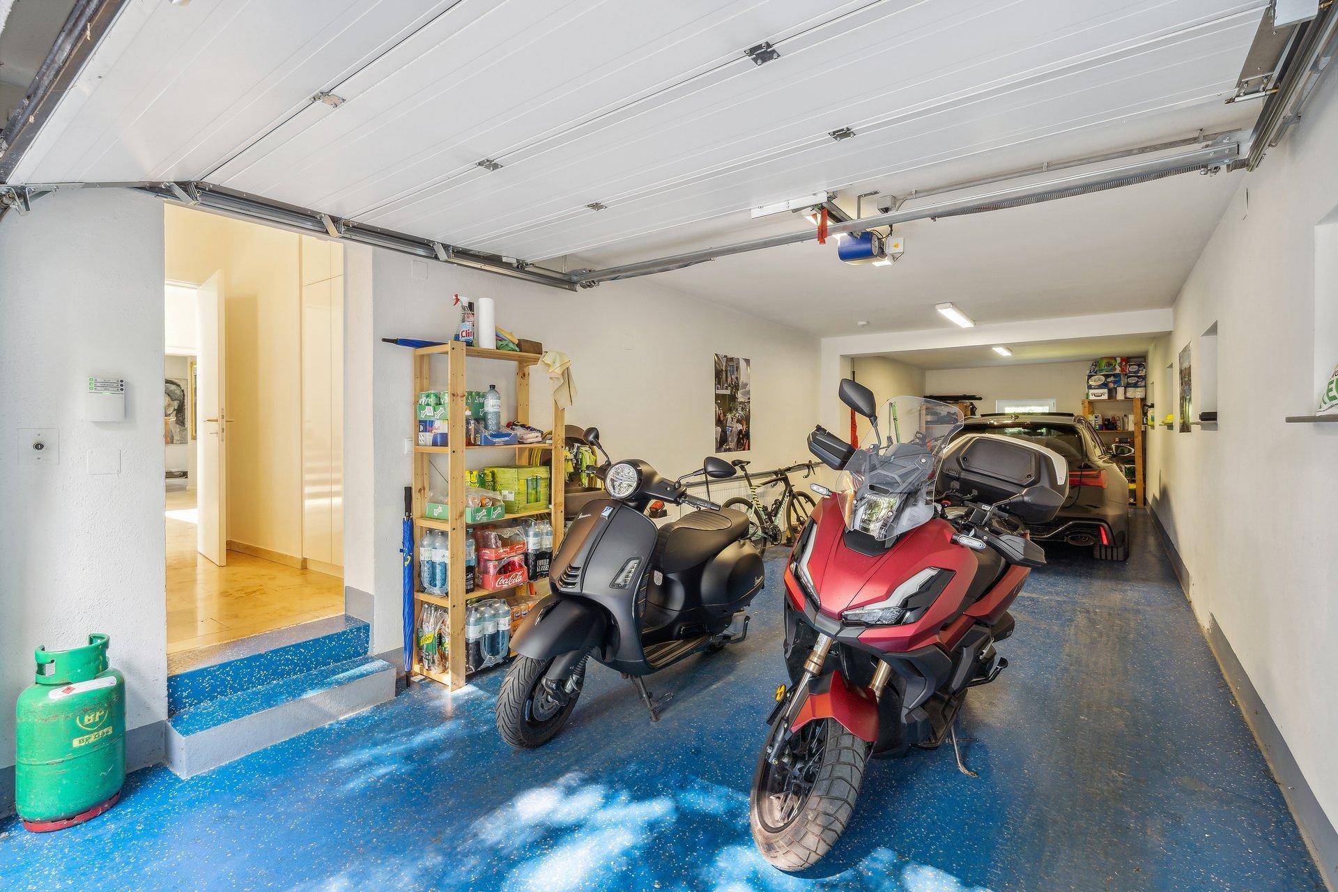 Geräumige Garage mit blauem Boden, Platz für Fahrzeuge und Stauraum.