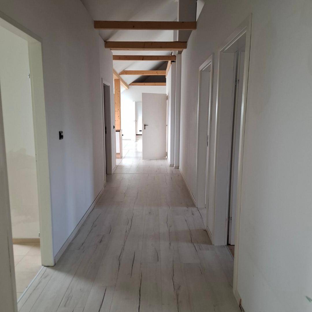 Heller Flur mit hellem Laminatboden, weißen Wänden und sichtbaren Holzdeckenbalken, der zu weiteren Räumen führt.