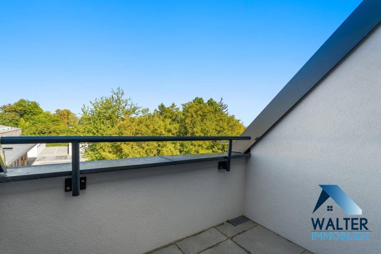 Kleiner Balkon mit Metallgeländer und Blick auf grüne Bäume und die Umgebung.