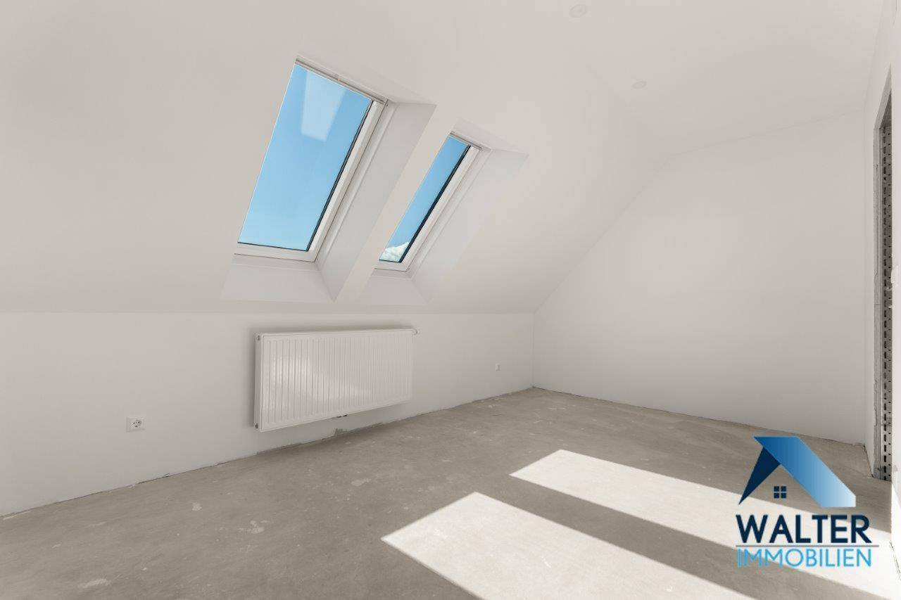 Dachzimmer mit schrägen Wänden, zwei Dachfenstern und viel Sonnenlicht auf dem Boden.