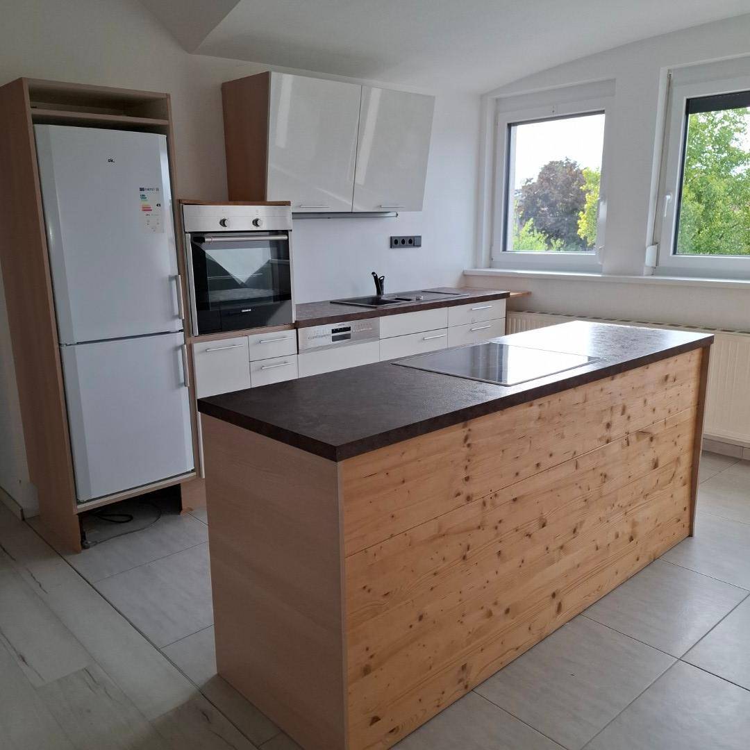 Moderne Küche mit Holzinsel, weißen Schränken, Einbaugeräten und Fenstern mit Blick ins Grüne.