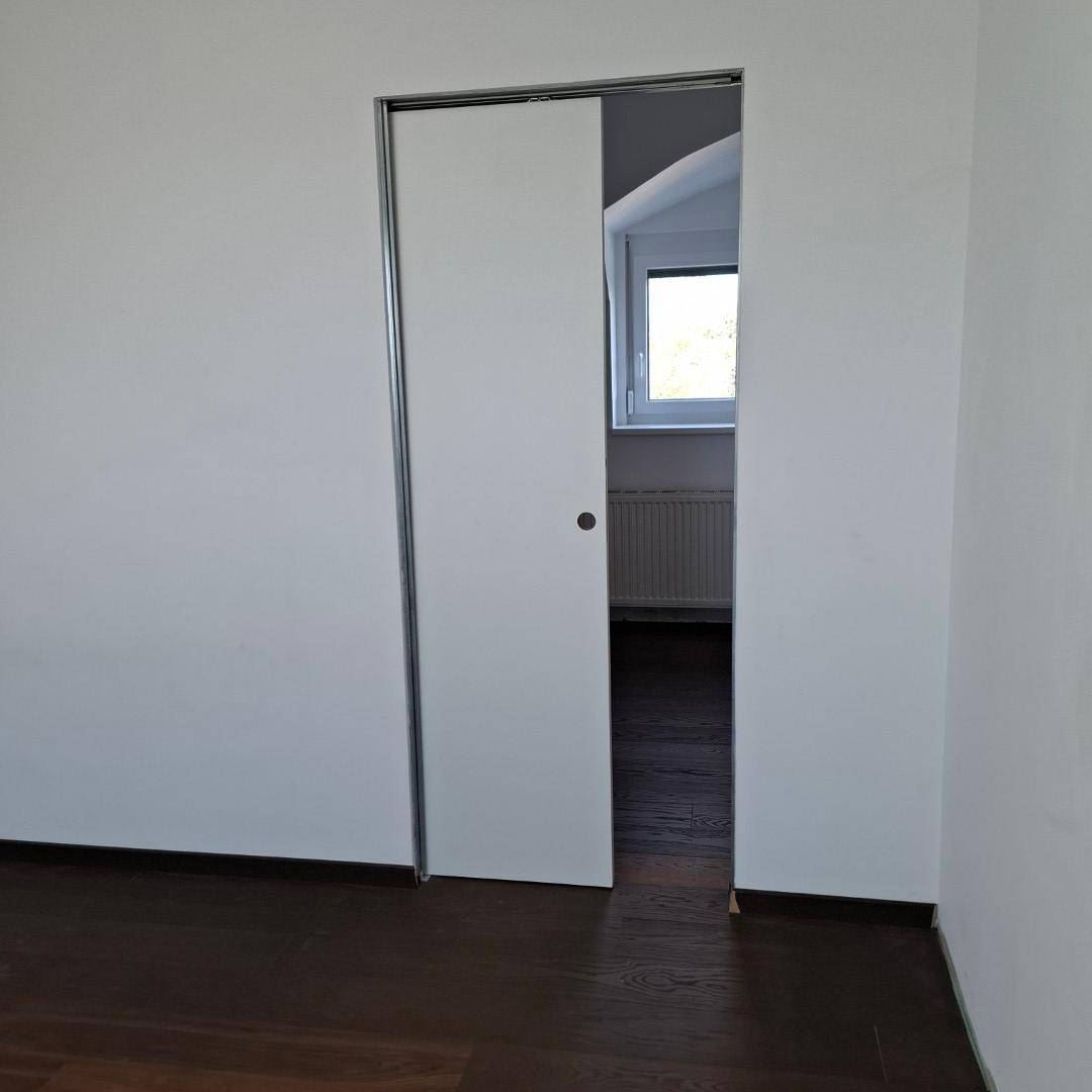 Zimmer mit dunklem Holzboden und einer modernen Schiebetür zum Nebenraum.