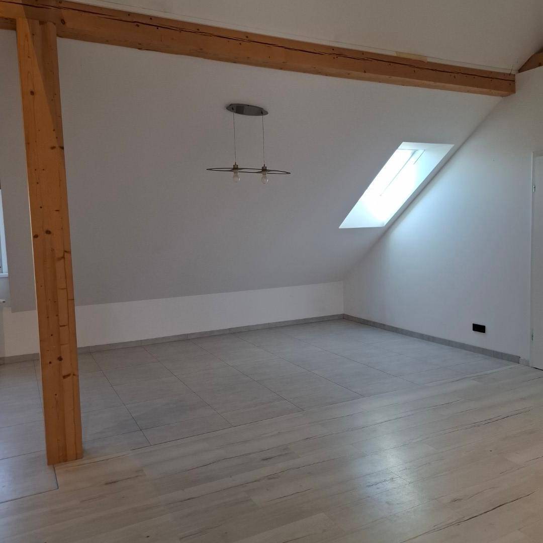 Heller Wohnbereich im Dachgeschoss mit Holzbalken, Dachschräge und Fliesenboden.