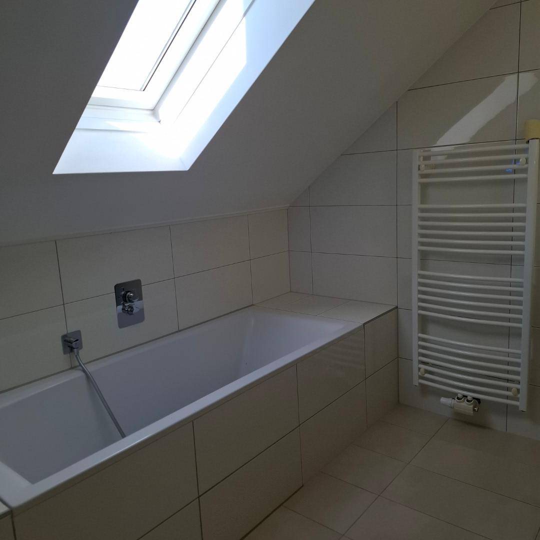 Helles Badezimmer im Dachgeschoss mit Badewanne, Dachfenster und Handtuchheizkörper.