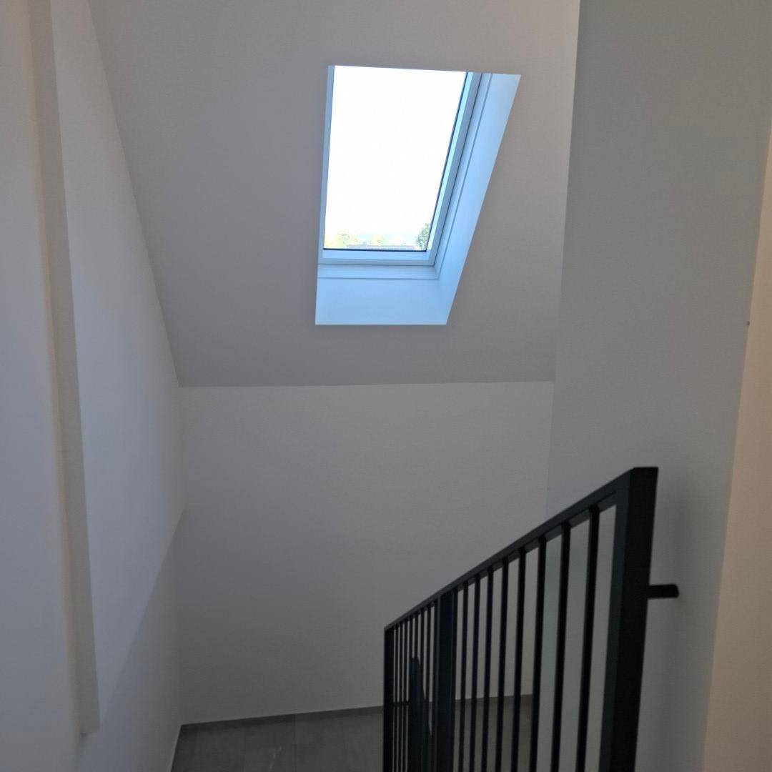 Treppenhaus mit modernem Geländer und einem Dachfenster, das Tageslicht spendet.