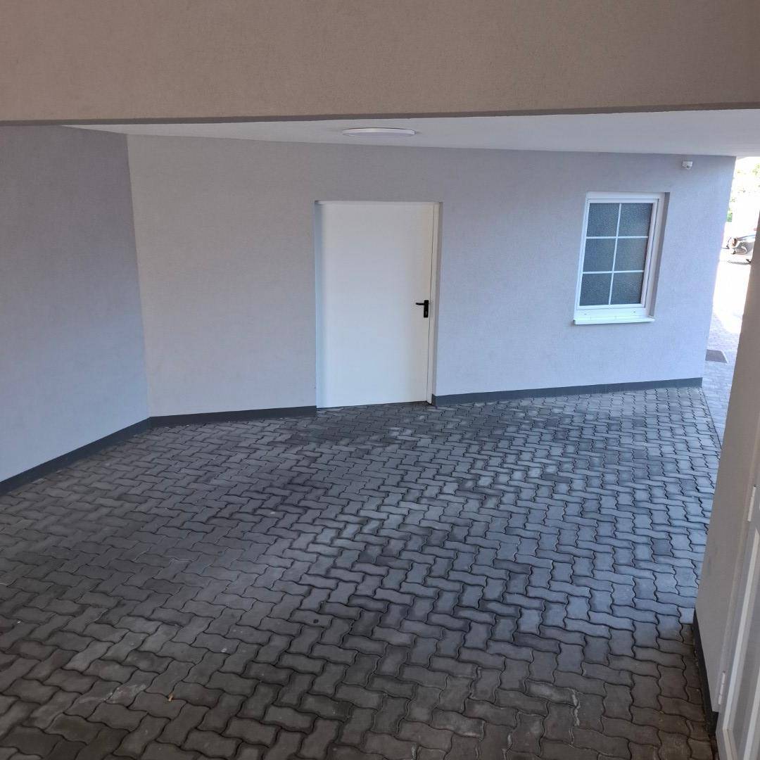 Überdachter Parkplatz mit Pflastersteinen und einer Tür, die in das Gebäude führt.