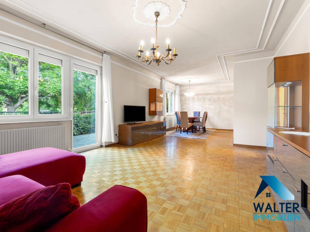 Geräumiger Wohn-Essbereich mit Parkettboden, Stuckdecke und Zugang zum Balkon.