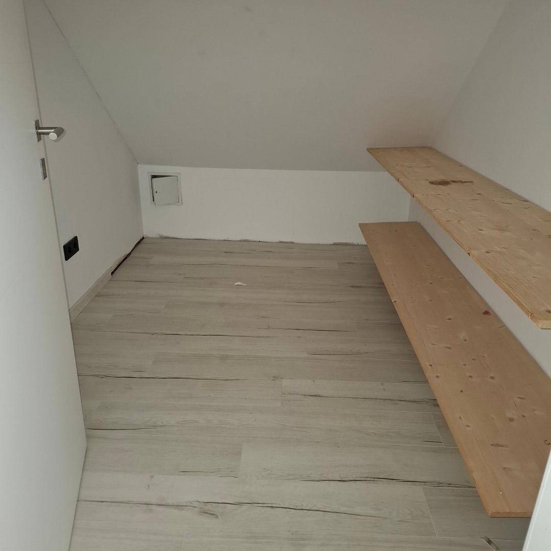 Kleiner Abstellraum mit hellem Laminatboden und zwei einfachen Holzregalen unter einer Dachschräge.