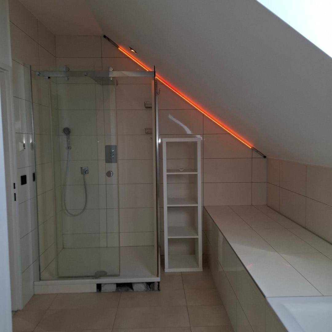 Modernes Badezimmer mit Duschkabine, Dachschräge und indirekter Beleuchtung in warmem Rot.