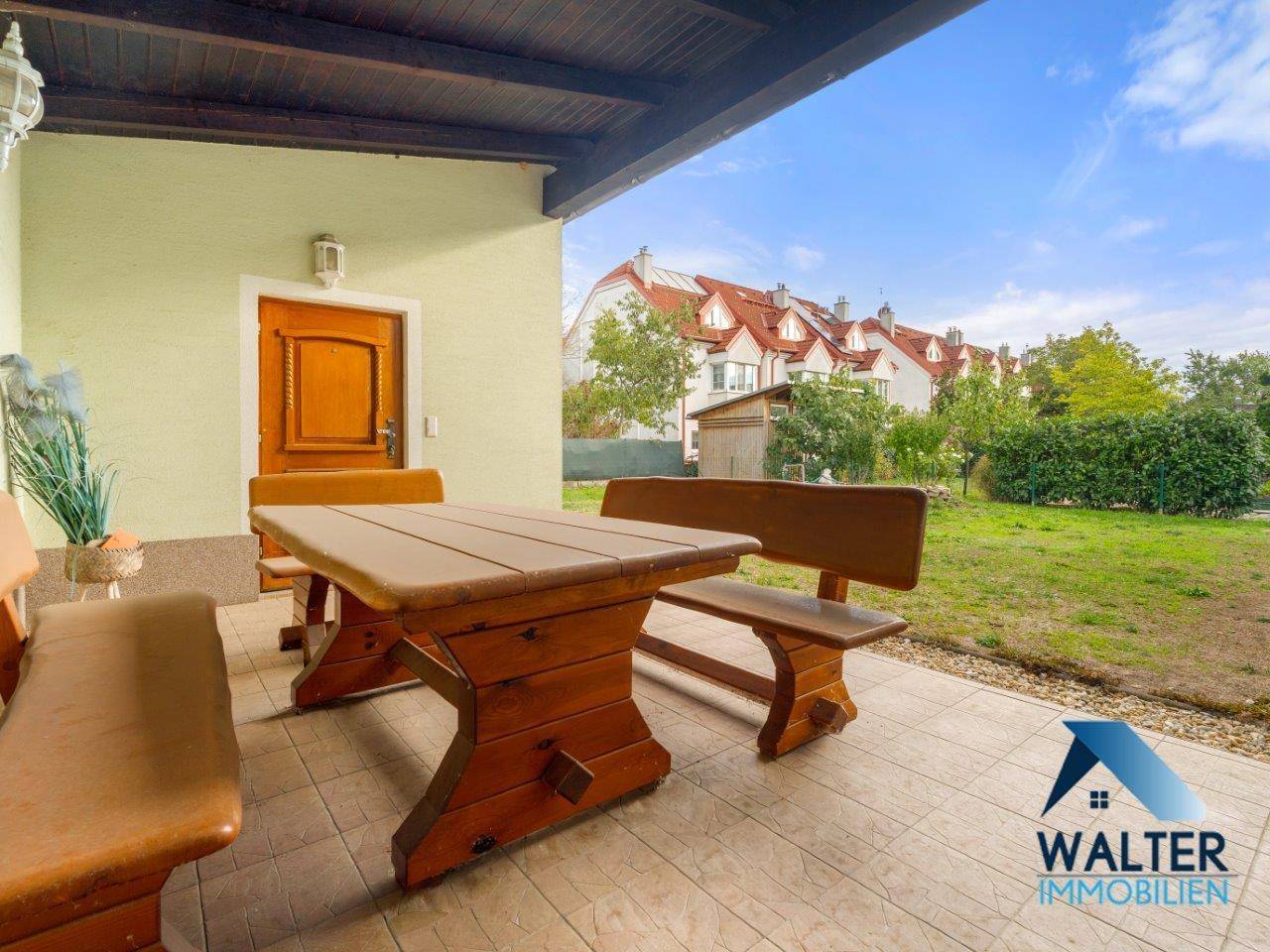 Gemütliche überdachte Terrasse mit Holztisch und Bänken, bietet Blick auf den grünen Garten.