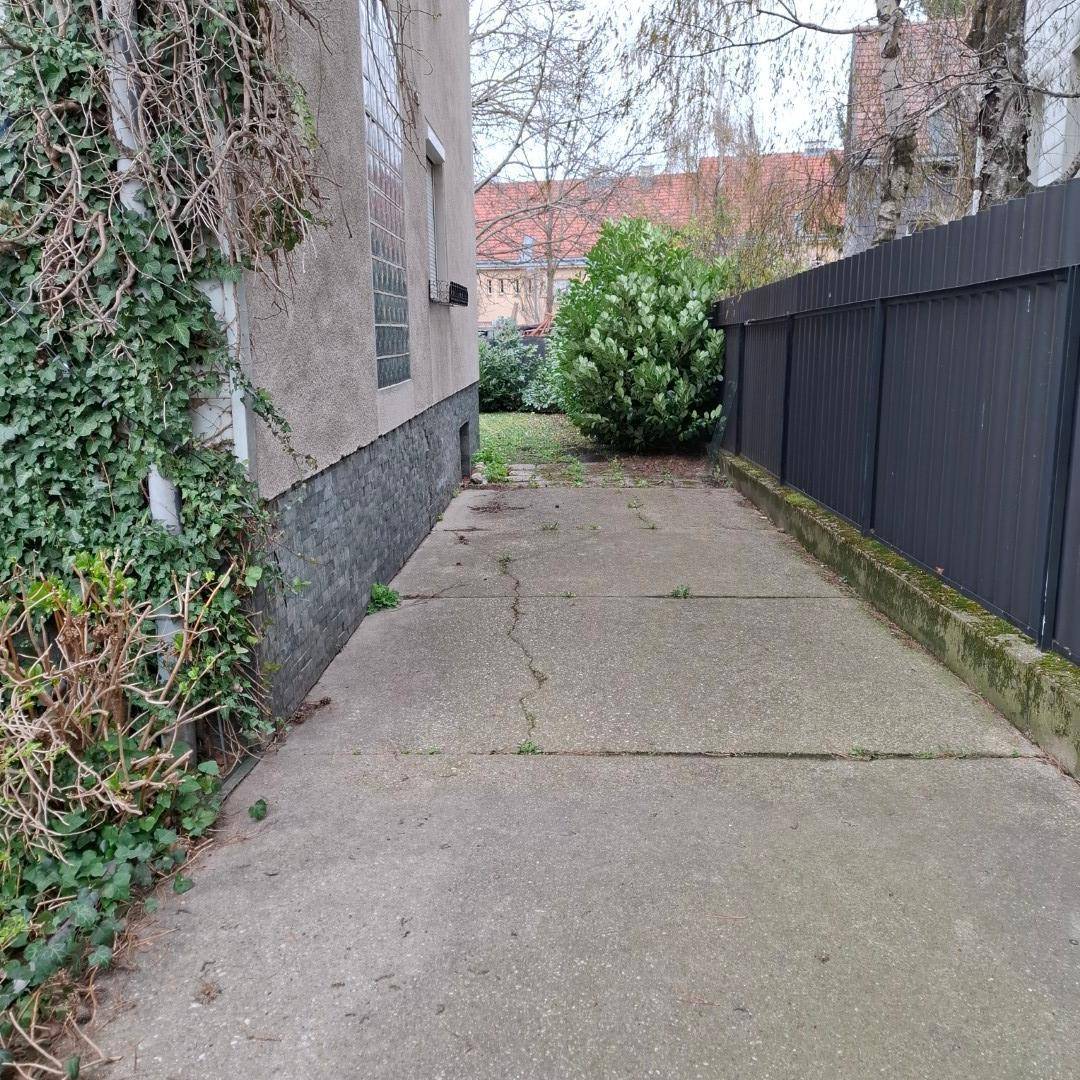 Seitlicher Zugang zum Haus mit gepflastertem Weg und grüner Bepflanzung.