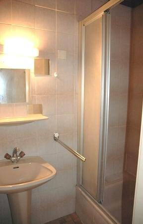 Badezimmer mit Waschbecken, Spiegel und Duschkabine, gefliest in hellen Farbtönen.