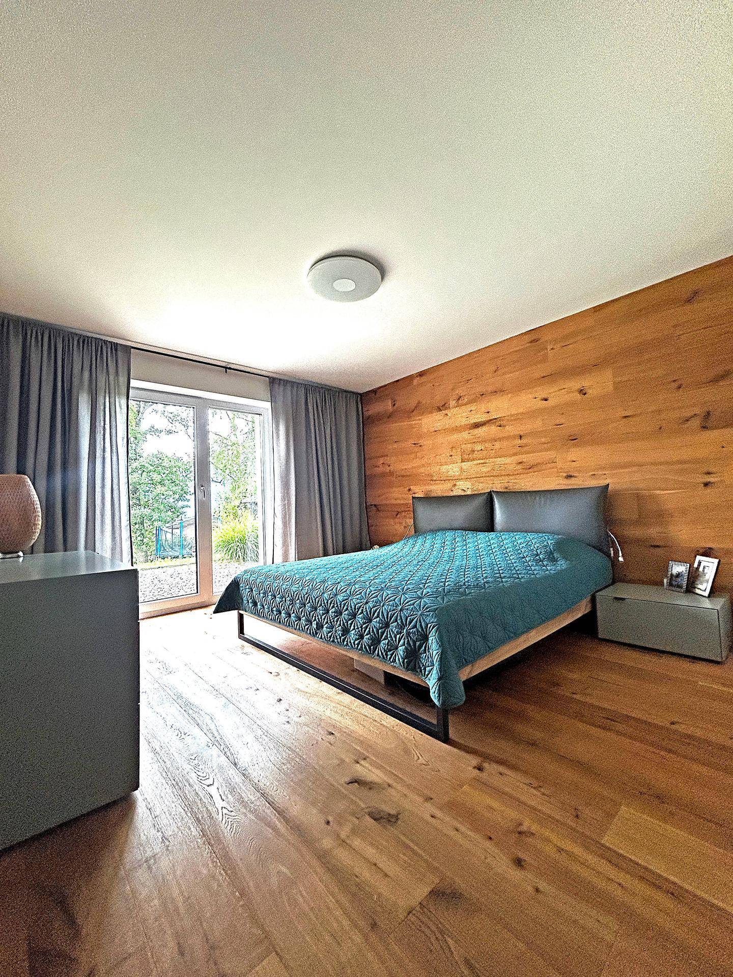Gemütliches Schlafzimmer mit Holzwand, Holzboden und Zugang zum Außenbereich.