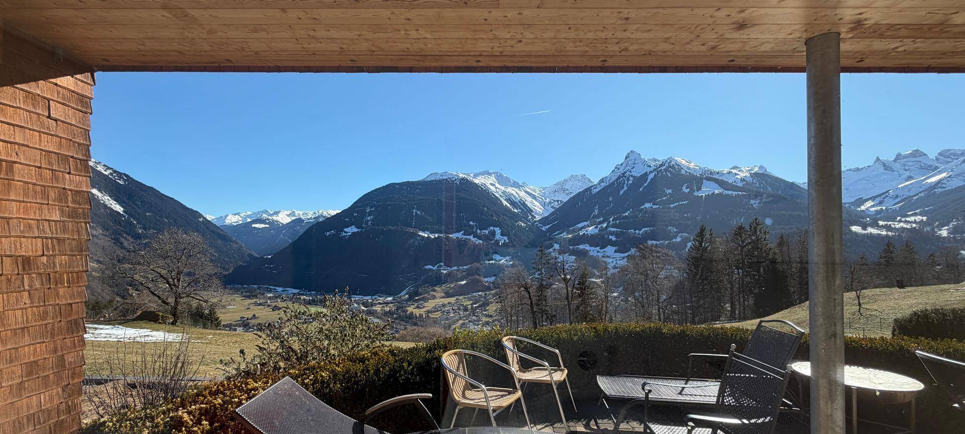 Überdachte Terrasse mit Sitzgelegenheiten und weitem Blick auf die schneebedeckten Berge und das Tal.