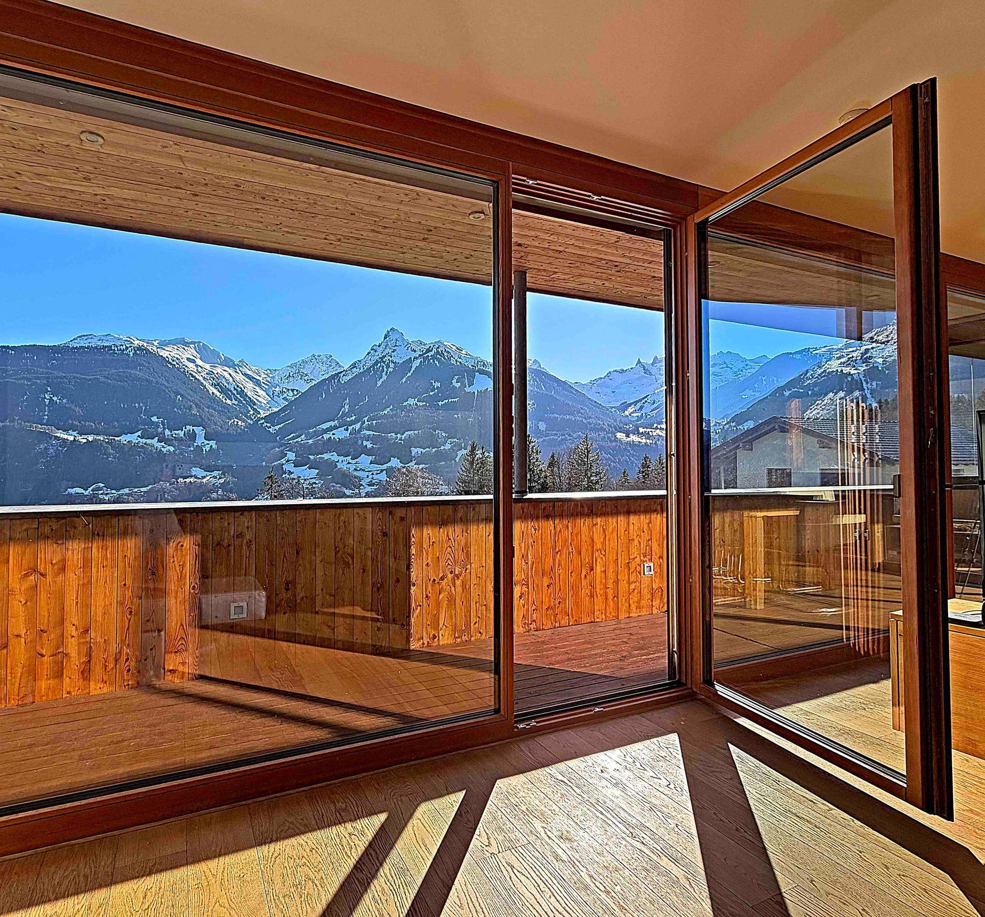 Heller Innenraum mit großen Glasfronten, die Zugang zu einem Balkon und einen weiten Bergblick bieten.