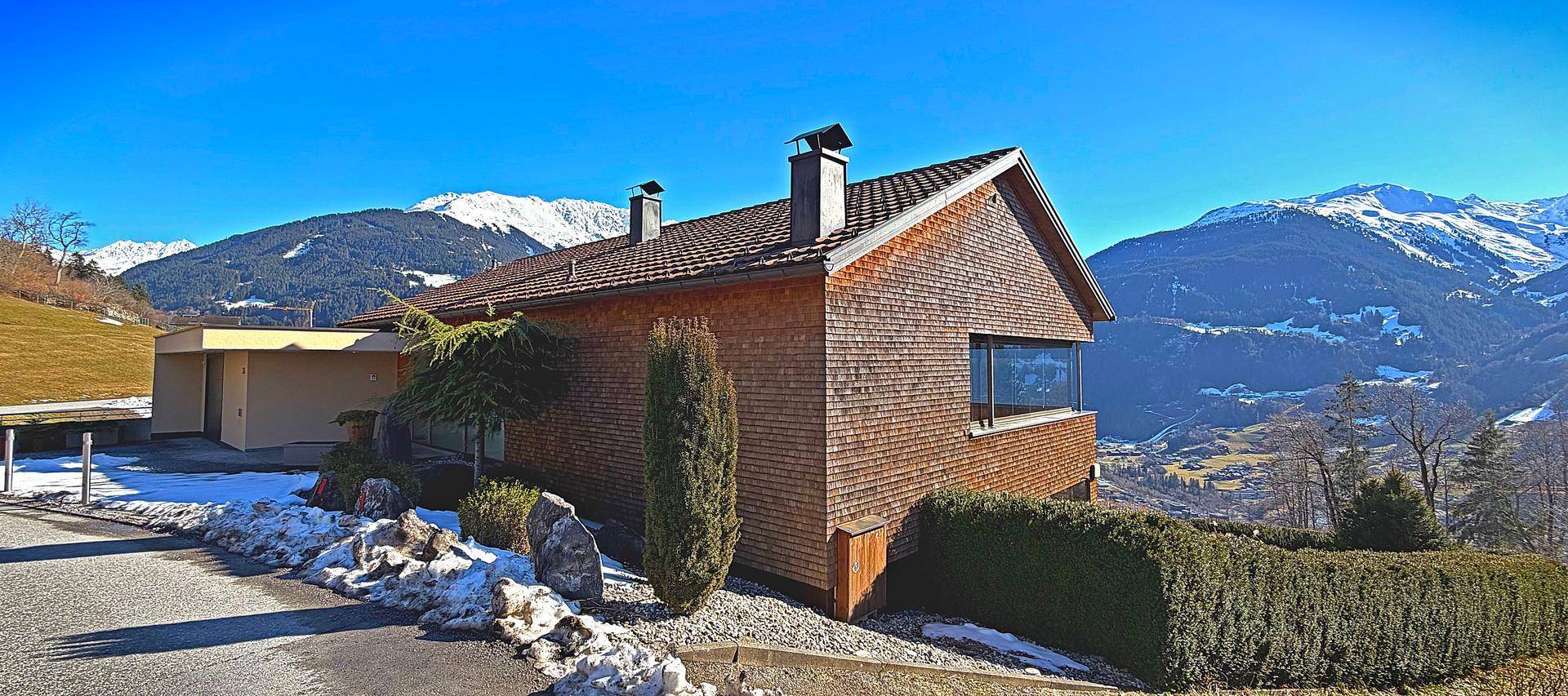 Charmantes Haus mit Holzschindelfassade und Satteldach, eingebettet in eine Berglandschaft mit Schnee.