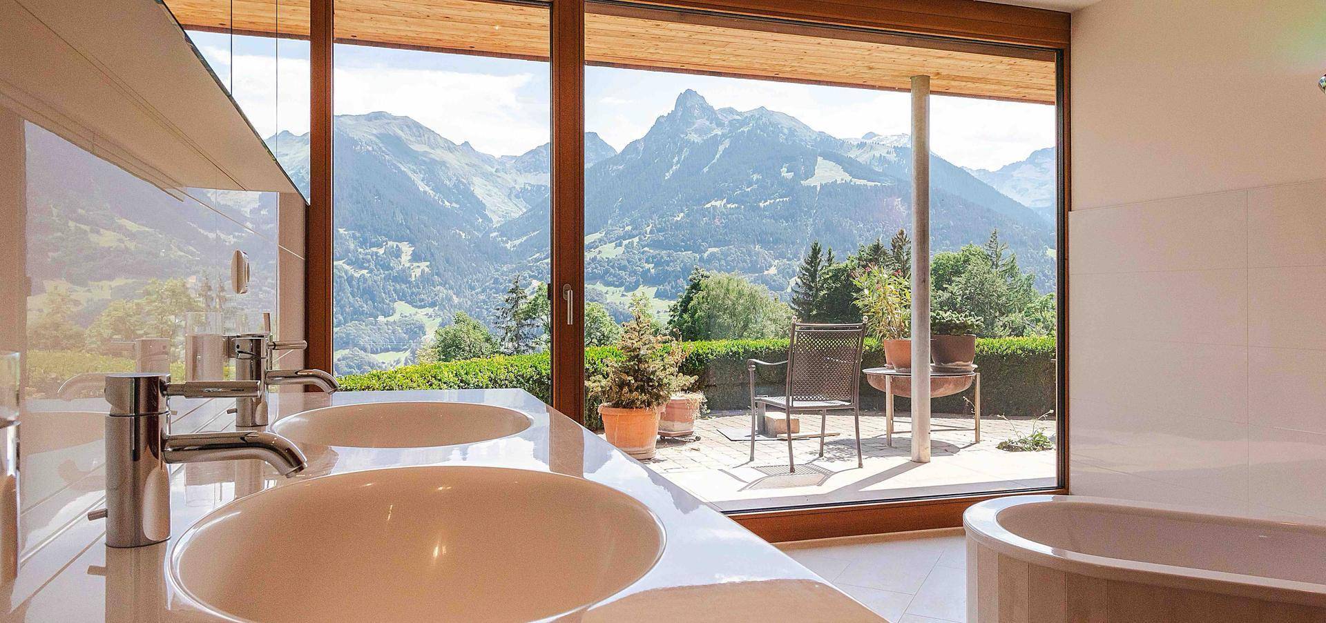 Modernes Badezimmer mit Doppelwaschbecken und raumhohen Fenstern mit Bergblick.