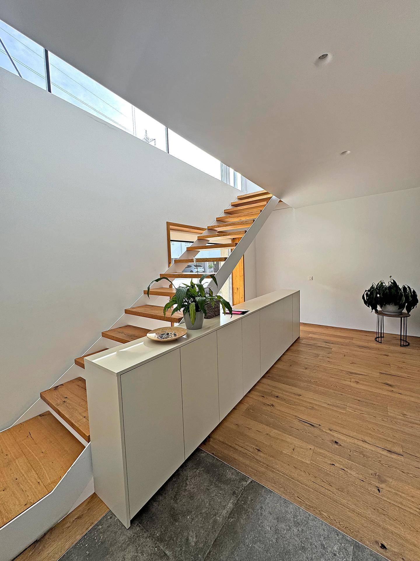 Heller Eingangsbereich mit moderner Holztreppe, Einbauschränken und Holzboden.