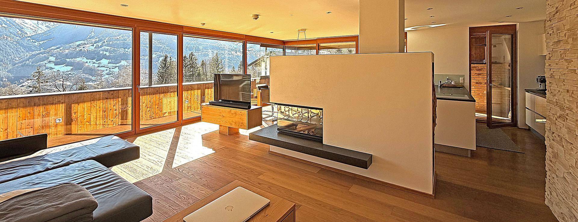 Helles Wohnzimmer mit Holzboden, Kamin und raumhohen Fenstern mit Bergblick.