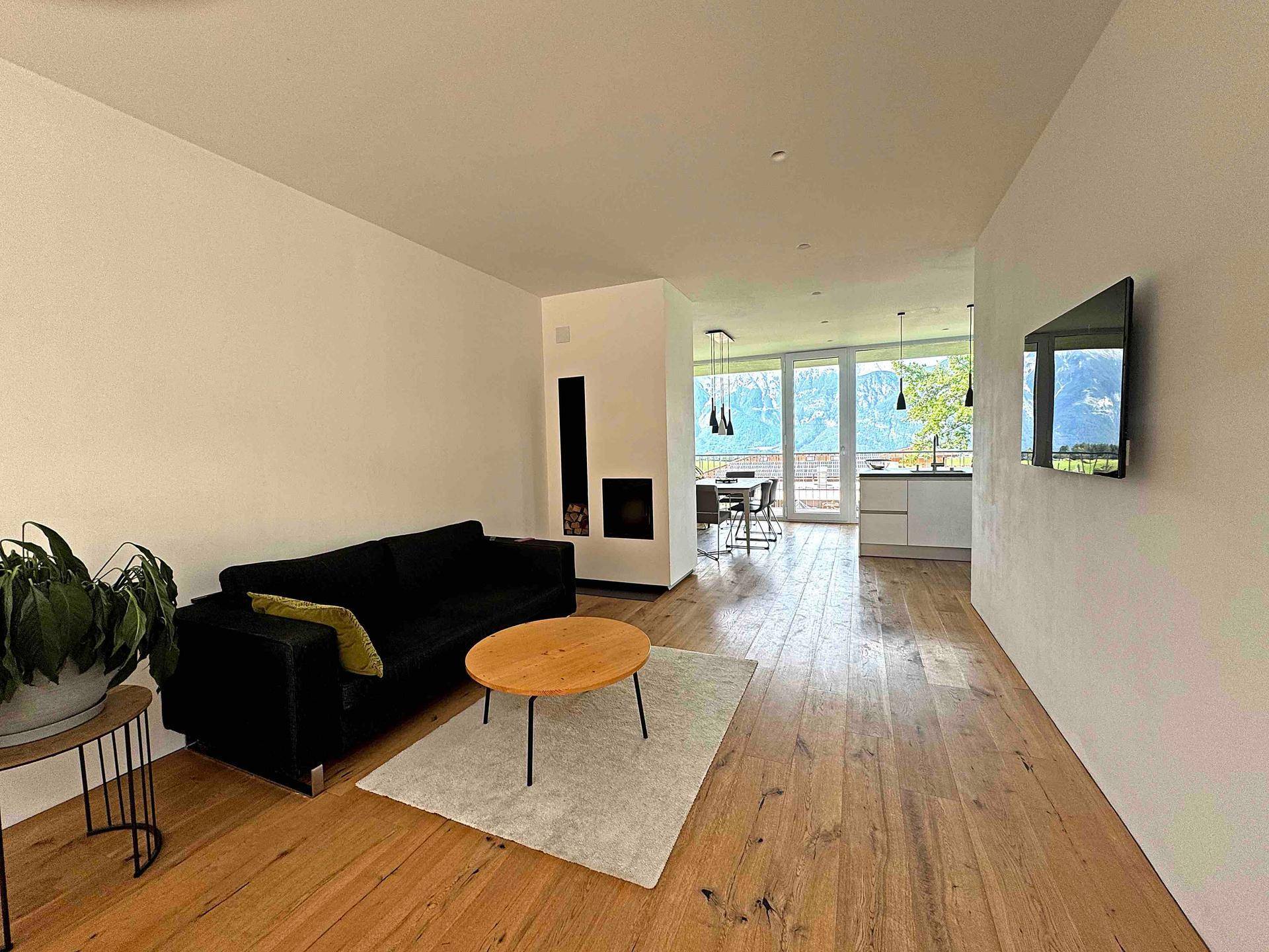 Gemütliches Wohnzimmer mit schwarzem Sofa, modernem Kamin und Holzboden mit Bergblick.