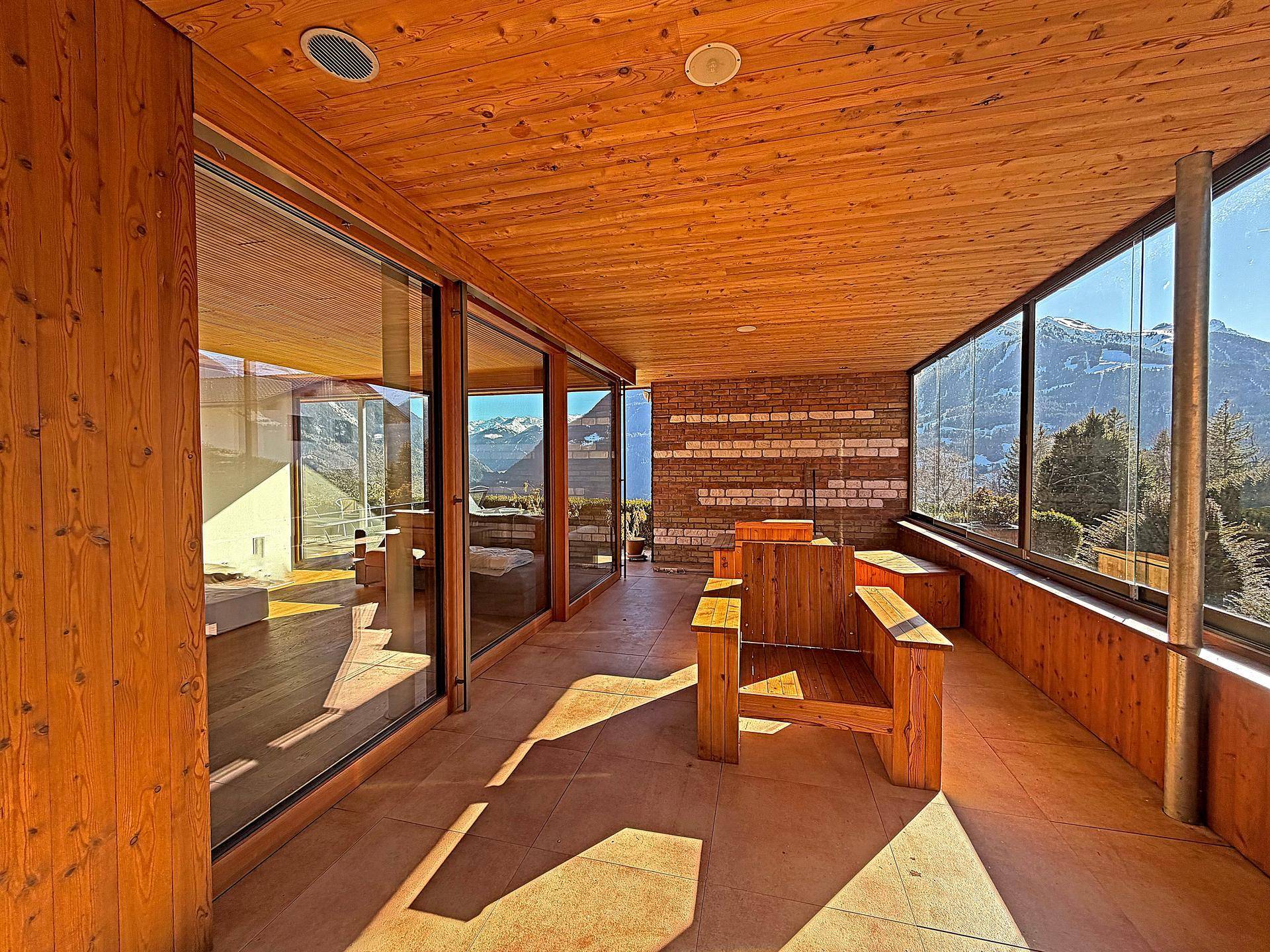 Gemütliche überdachte Loggia mit Holzboden und -decke, ausgestattet mit Sitzgelegenheiten und Bergblick.