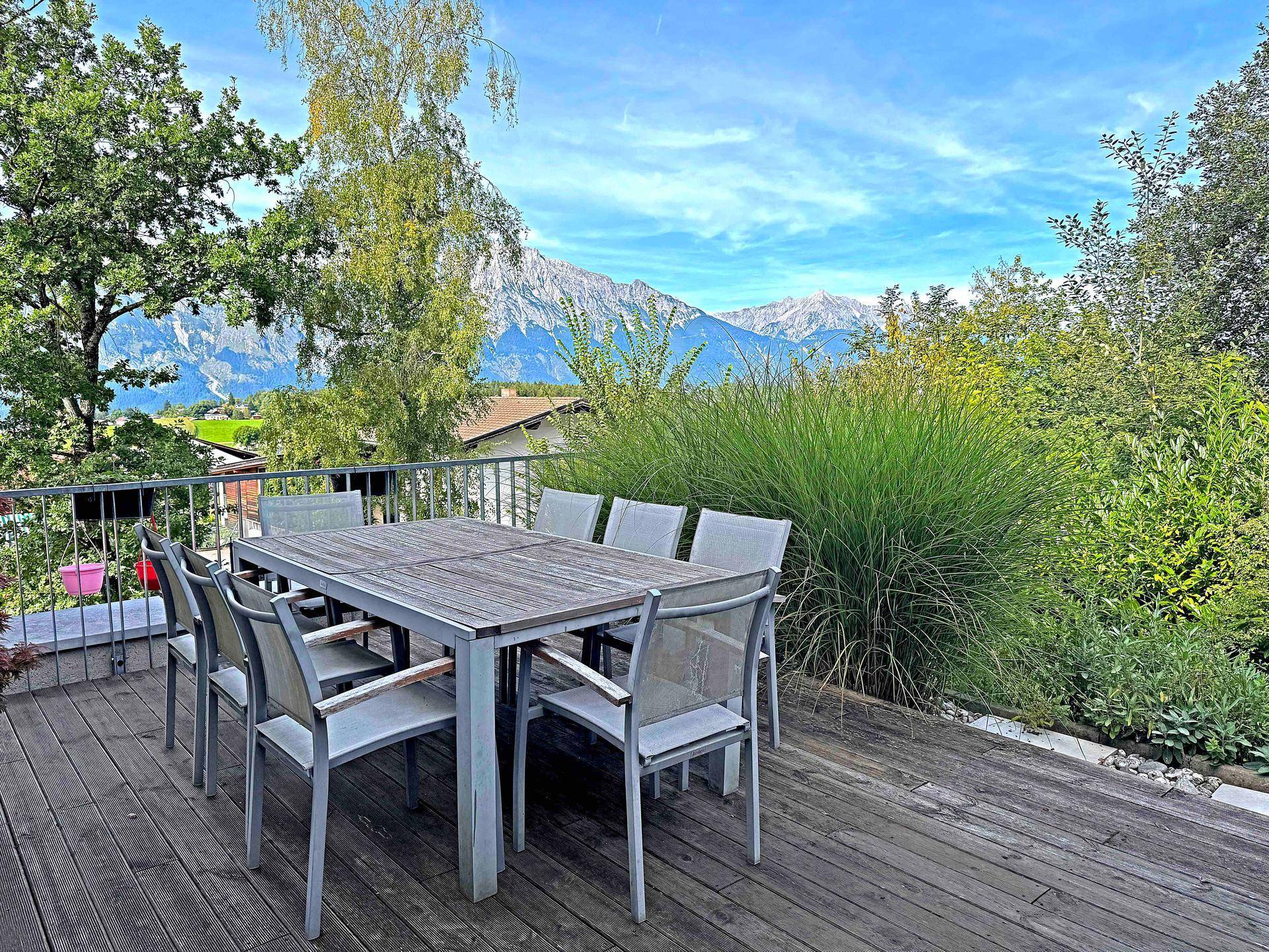 Geräumige Terrasse mit Esstisch und Stühlen, umgeben von Pflanzen und mit Bergblick.
