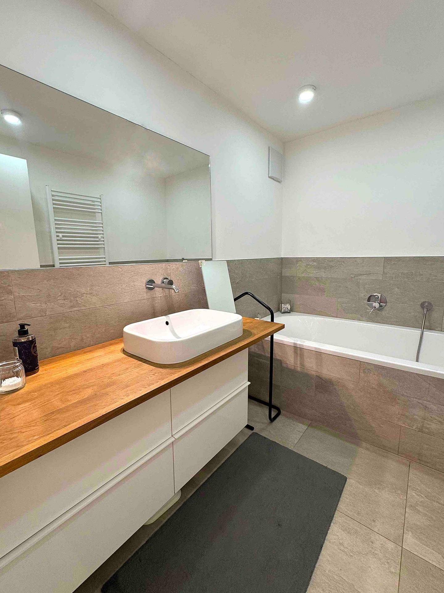 Modernes Badezimmer mit Aufsatzwaschbecken, Holzwaschtisch, Badewanne und beheiztem Handtuchhalter.
