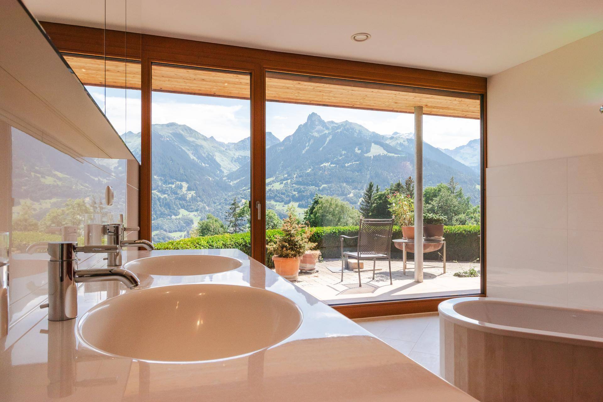 Modernes Badezimmer mit Doppelwaschbecken, Badewanne und Zugang zur Terrasse mit Bergblick.