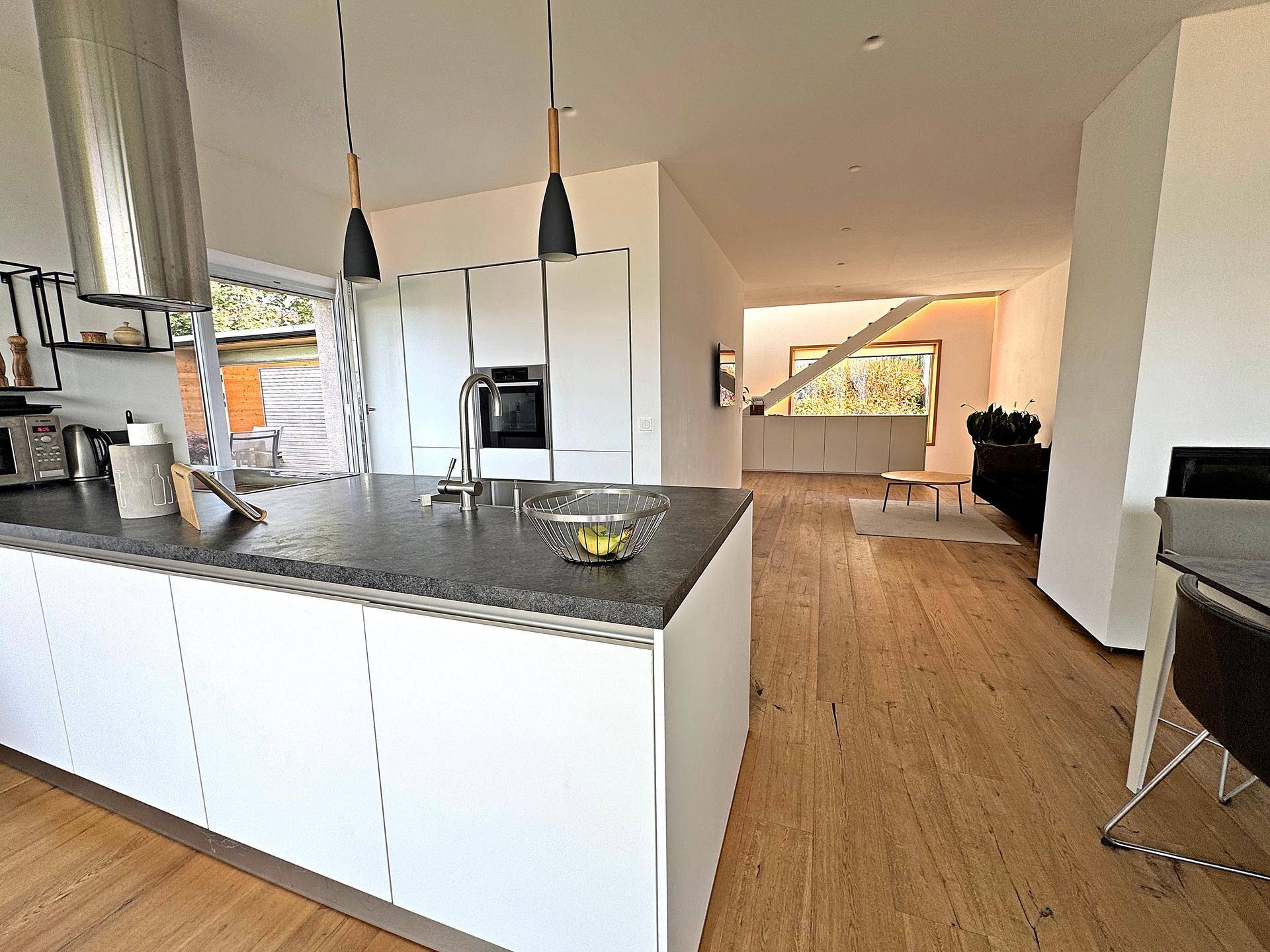 Moderne offene Küche mit Kücheninsel, dunkler Arbeitsplatte und Blick auf den Wohnbereich.