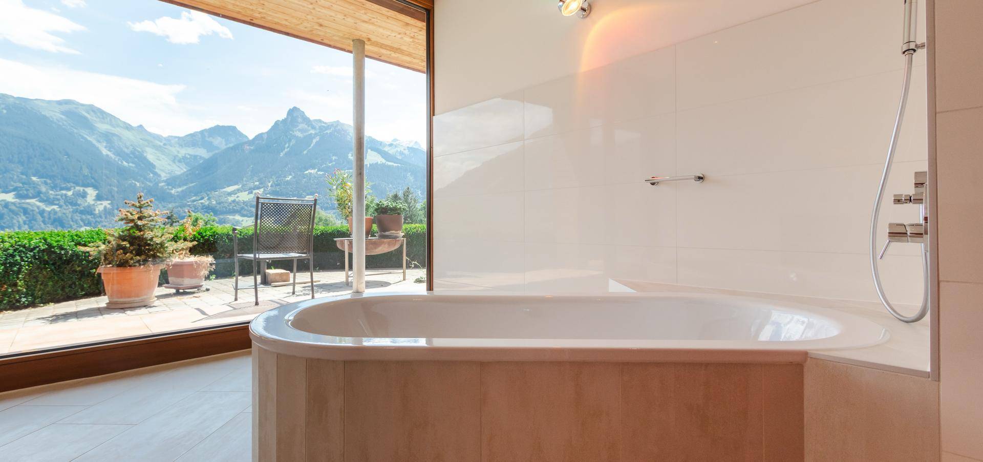 Helles Badezimmer mit Badewanne, Dusche und direktem Blick auf die umliegende Berglandschaft.
