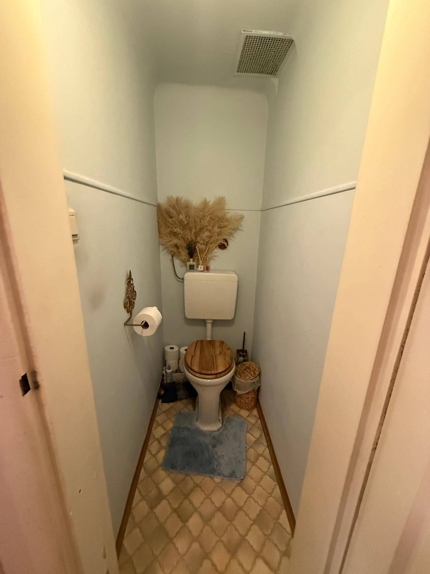 Kleines Gäste-WC mit Toilette, Holz-Toilettensitz und einem Lüftungsgitter.