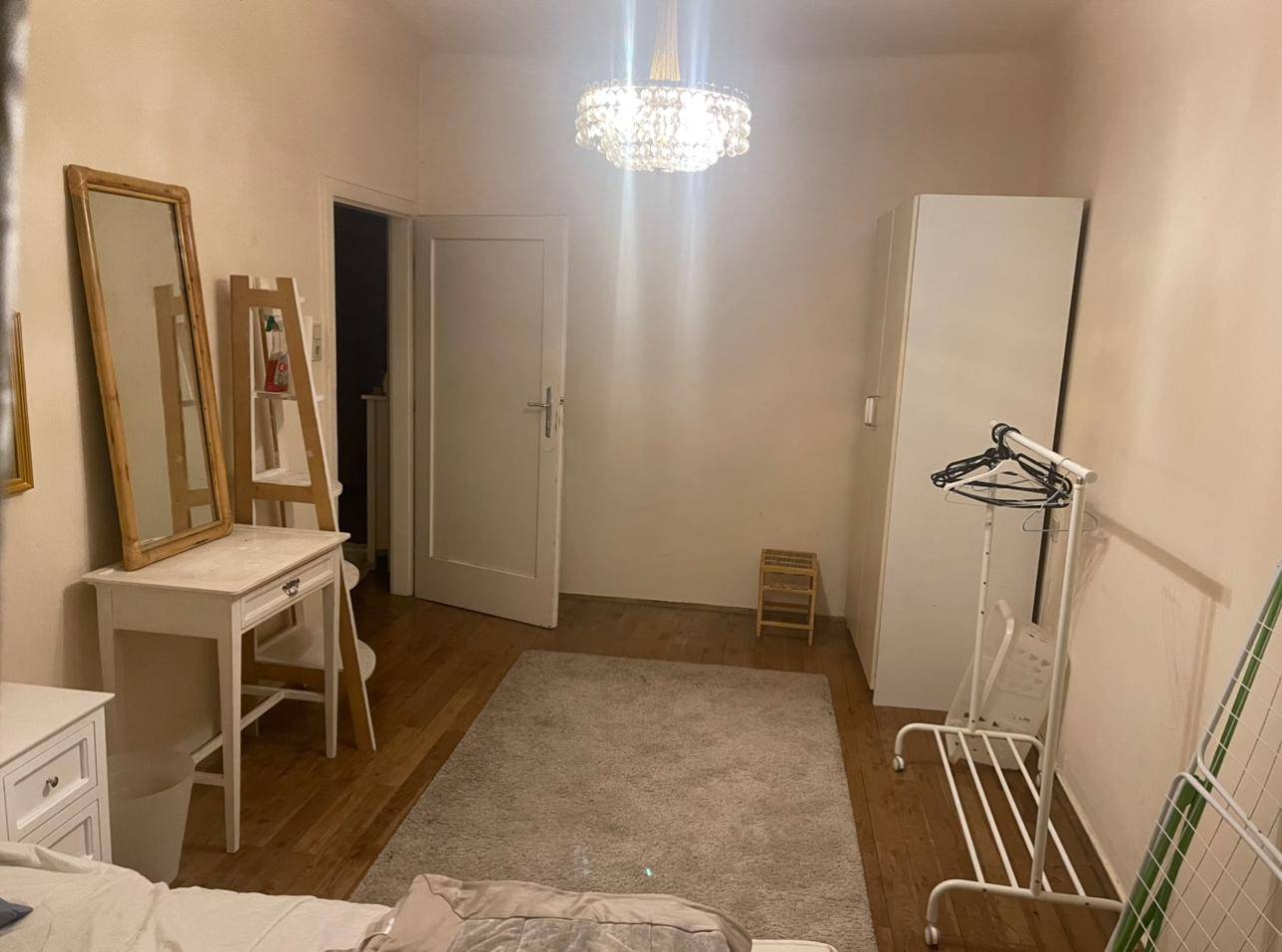 Schlafzimmer mit Holzboden, weißem Kleiderschrank, Kleiderständer und einer Tür.