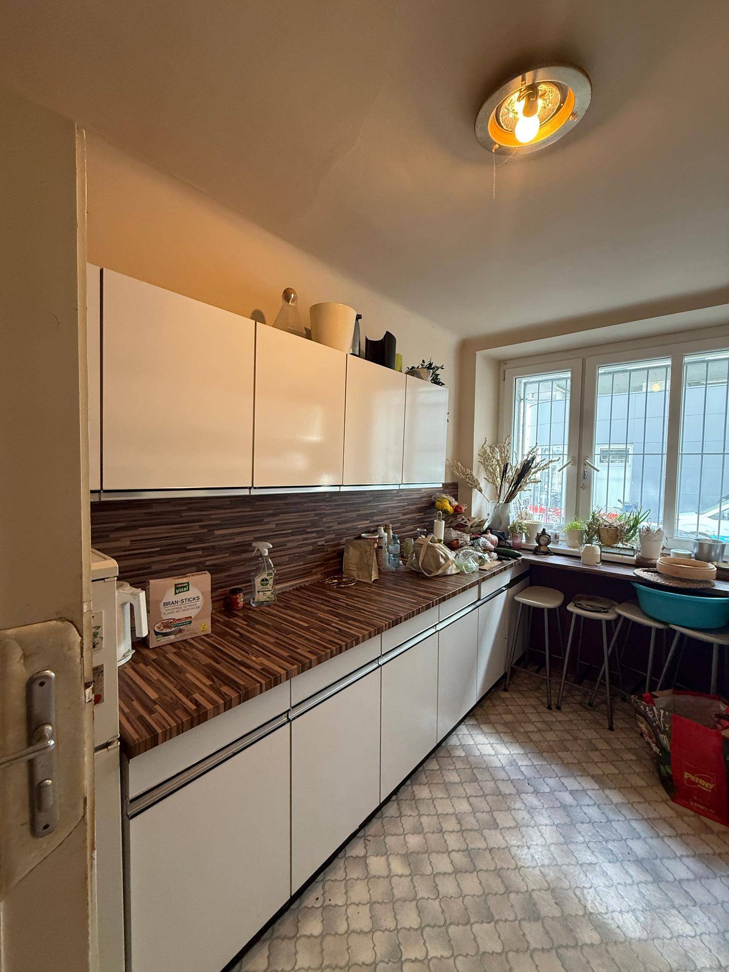 Helle Küche mit weißen Schränken, Holzarbeitsplatten und einem großen Fenster.