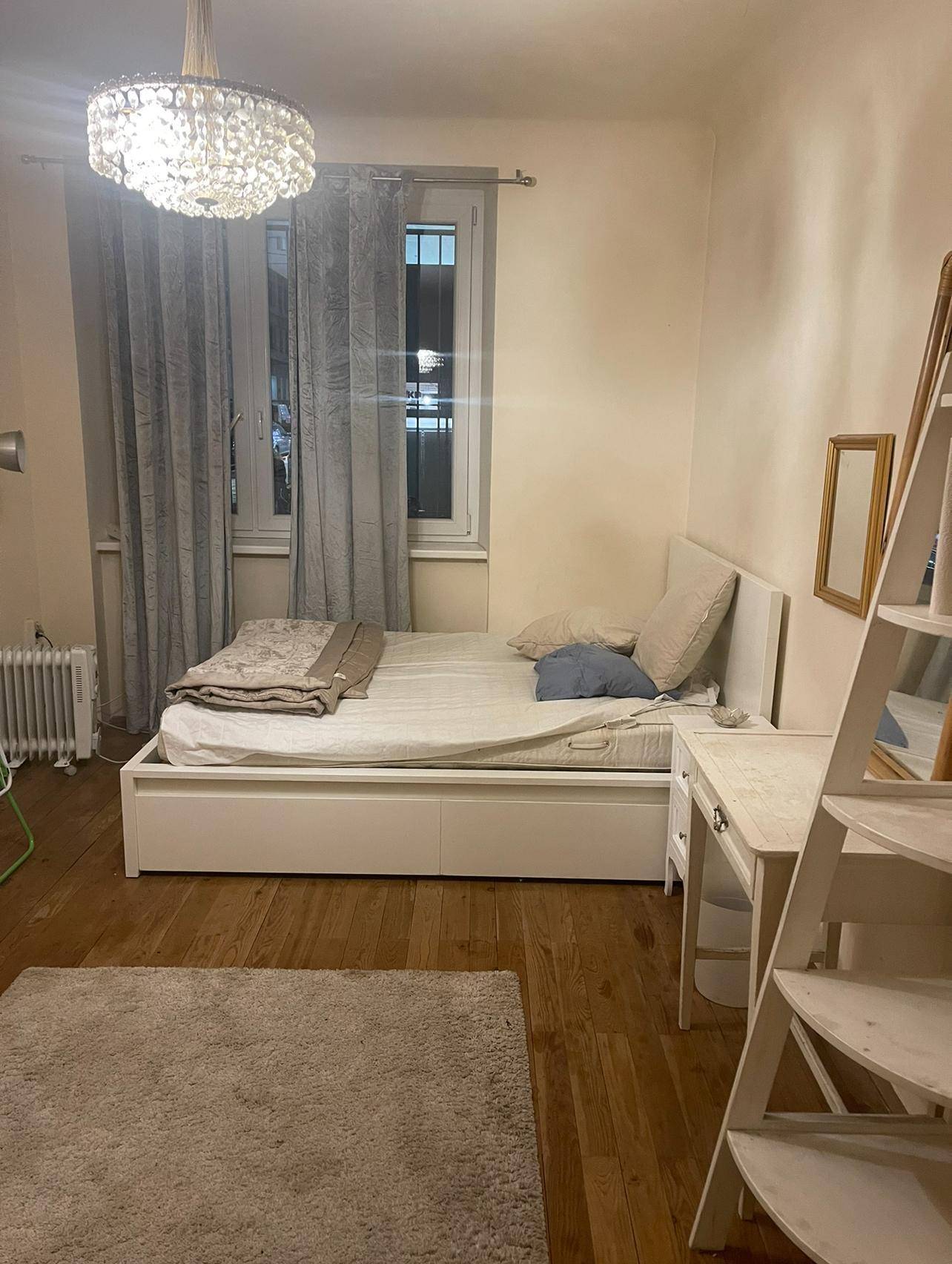Schlafzimmer mit Holzboden, Bett, Fenster mit Vorhängen und einem kleinen Schreibtisch.