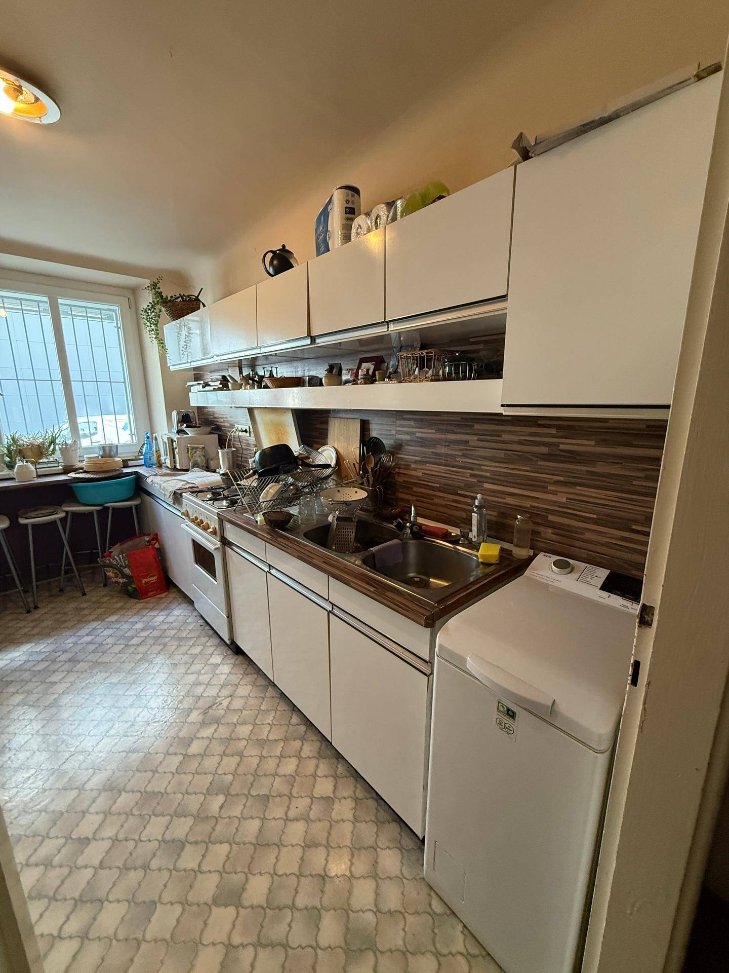 Funktionale Küche mit weißen Schränken, Spüle, Herd und einer Waschmaschine.