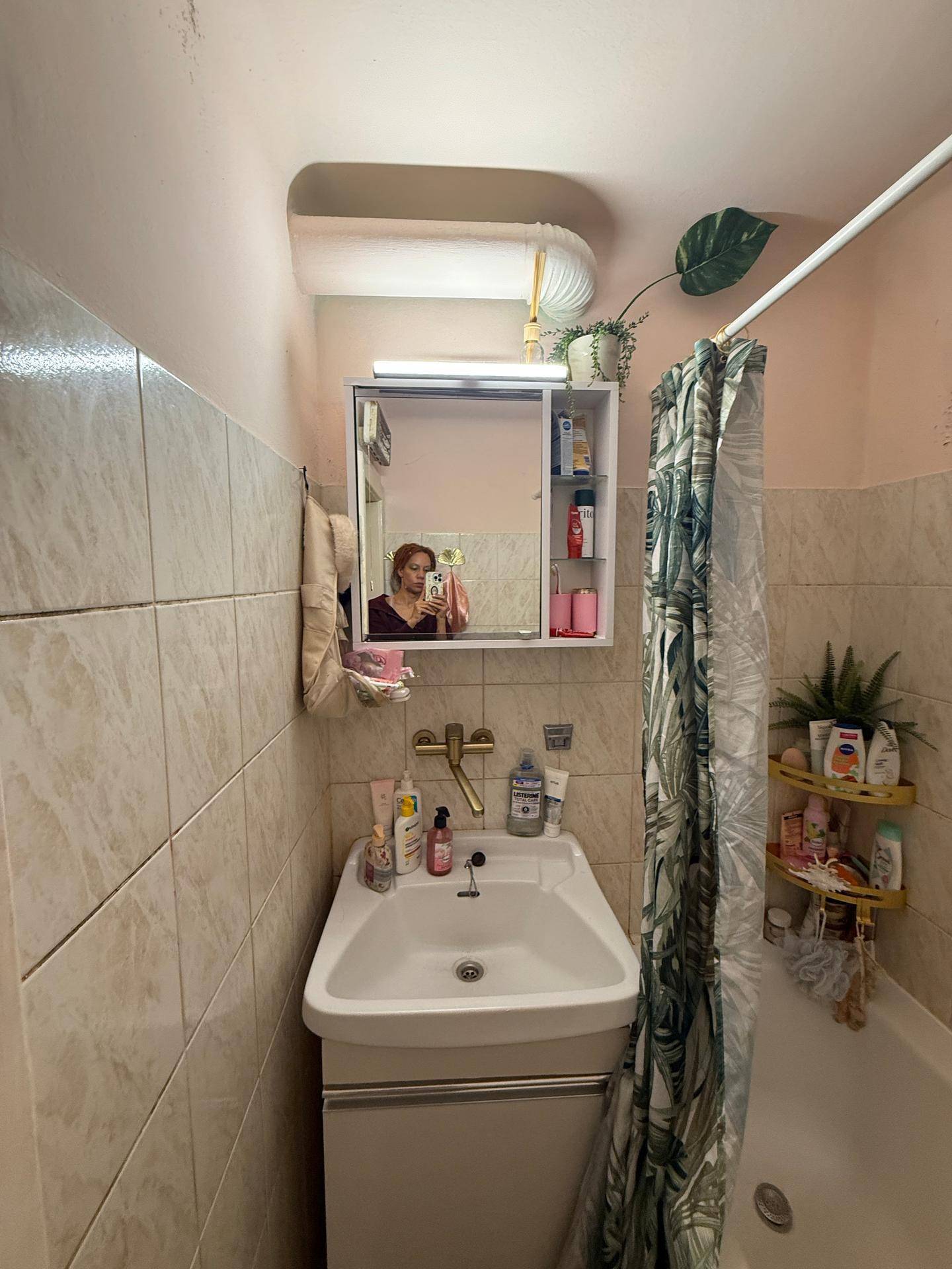 Badezimmer mit Waschbecken, Spiegelschrank und Fliesen, bietet grundlegende Hygieneausstattung.
