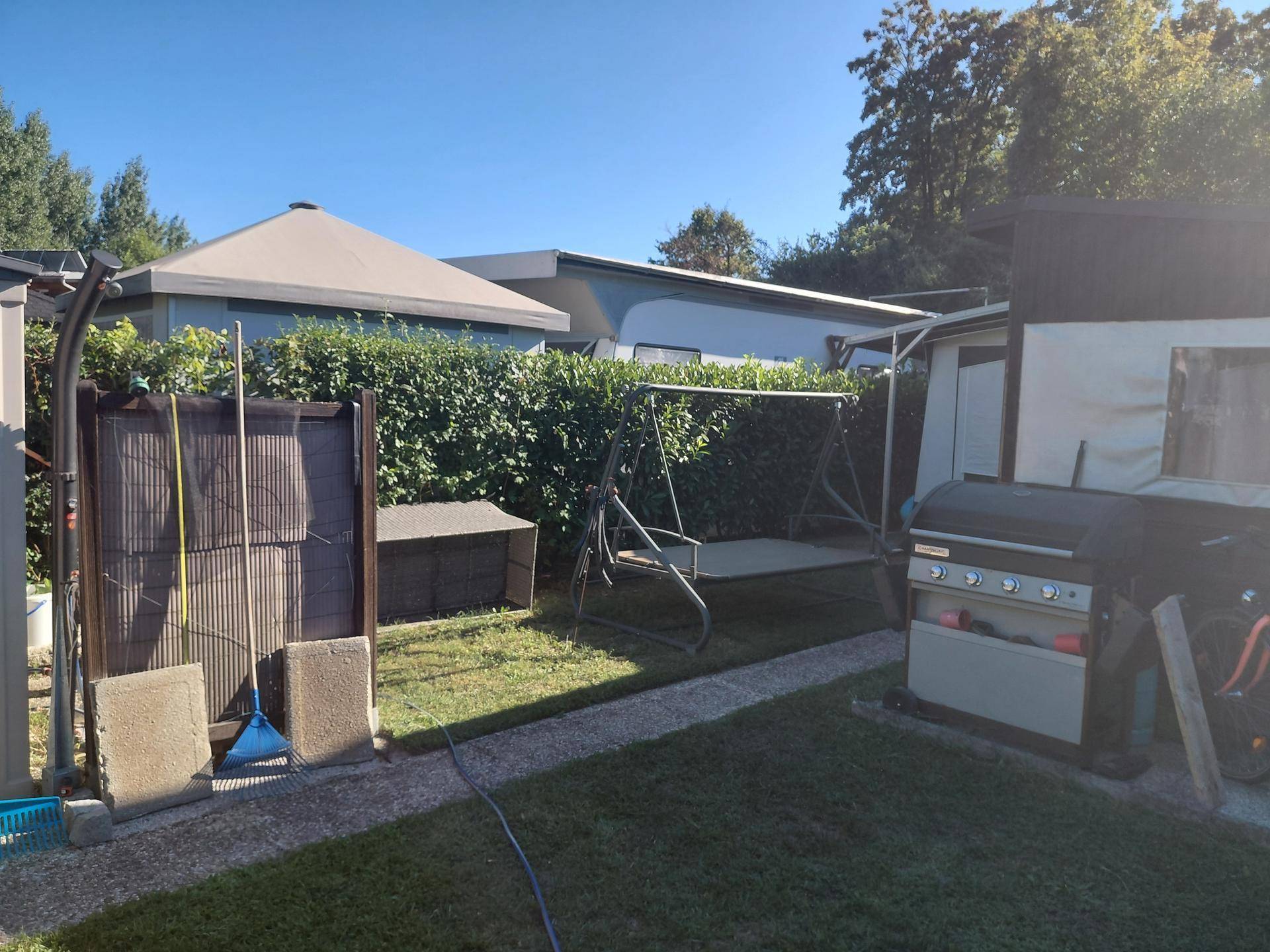 Gartenbereich mit einer Hollywoodschaukel, Grill und einem kleinen Schuppen, umgeben von Hecken.