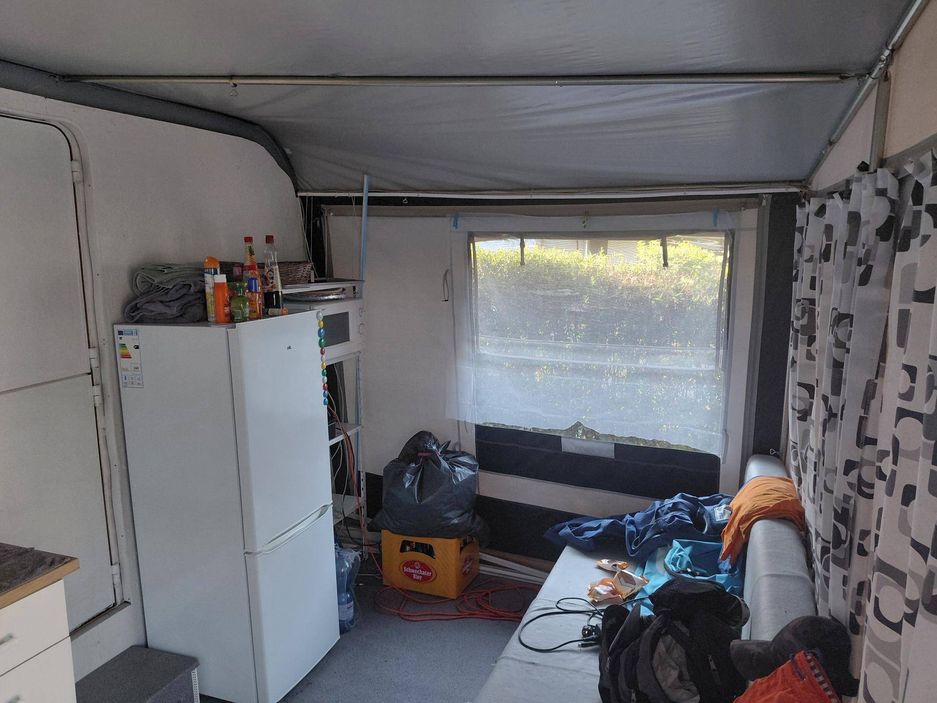 Wohnbereich mit Sofa, Kühlschrank und einem Fenster, das Tageslicht hereinlässt.