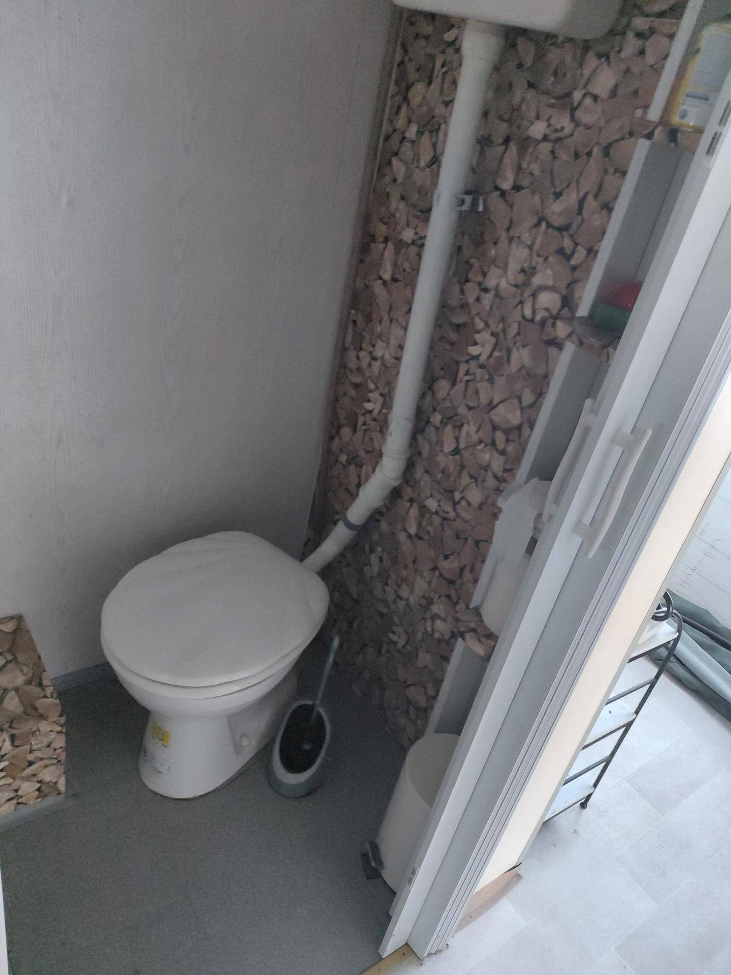Kleines WC mit einfacher Toilette und sichtbaren Rohrleitungen in einem kompakten Raum.