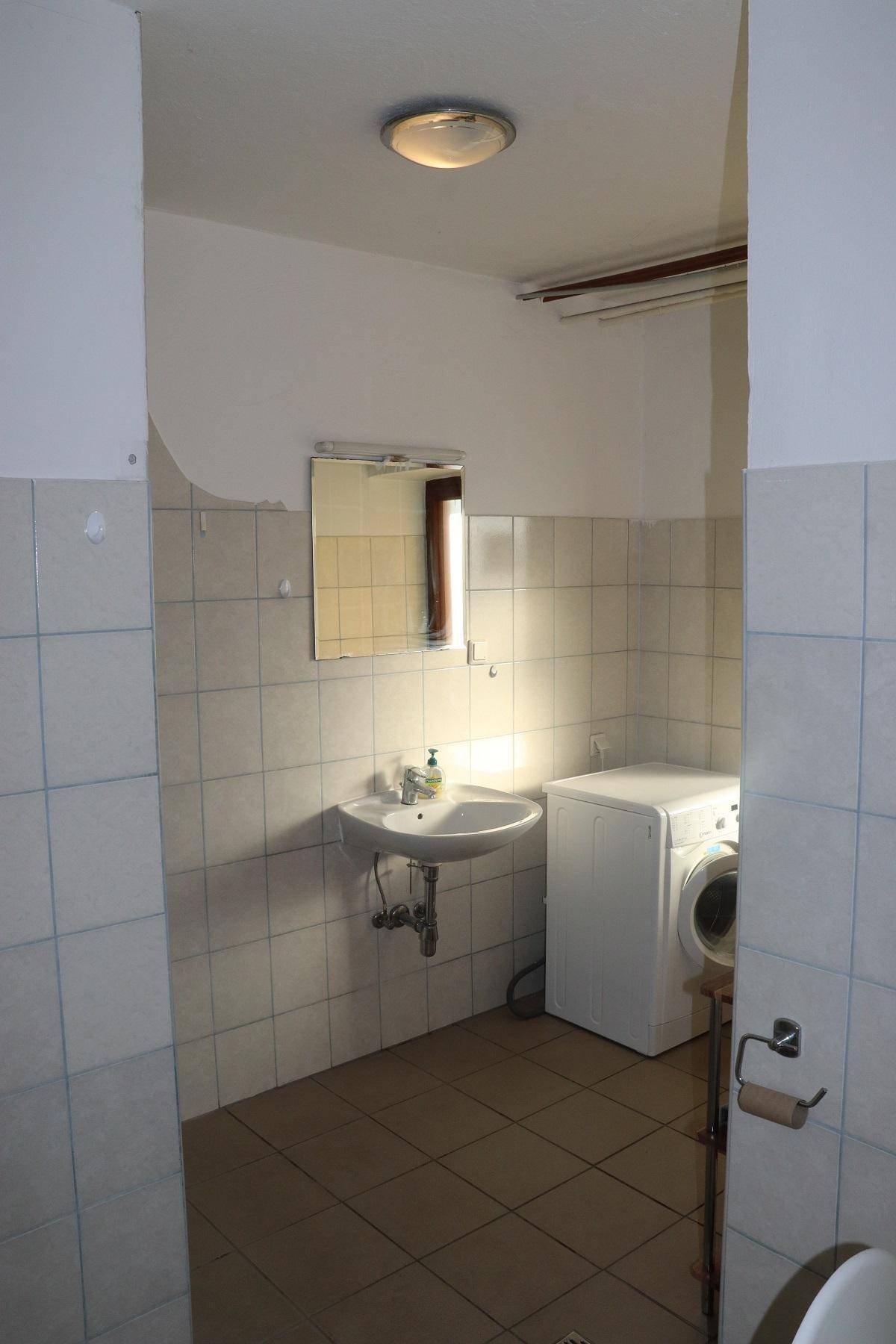 Funktionales Badezimmer mit Waschbecken, Spiegel und einer Waschmaschine, teilweise gefliest.