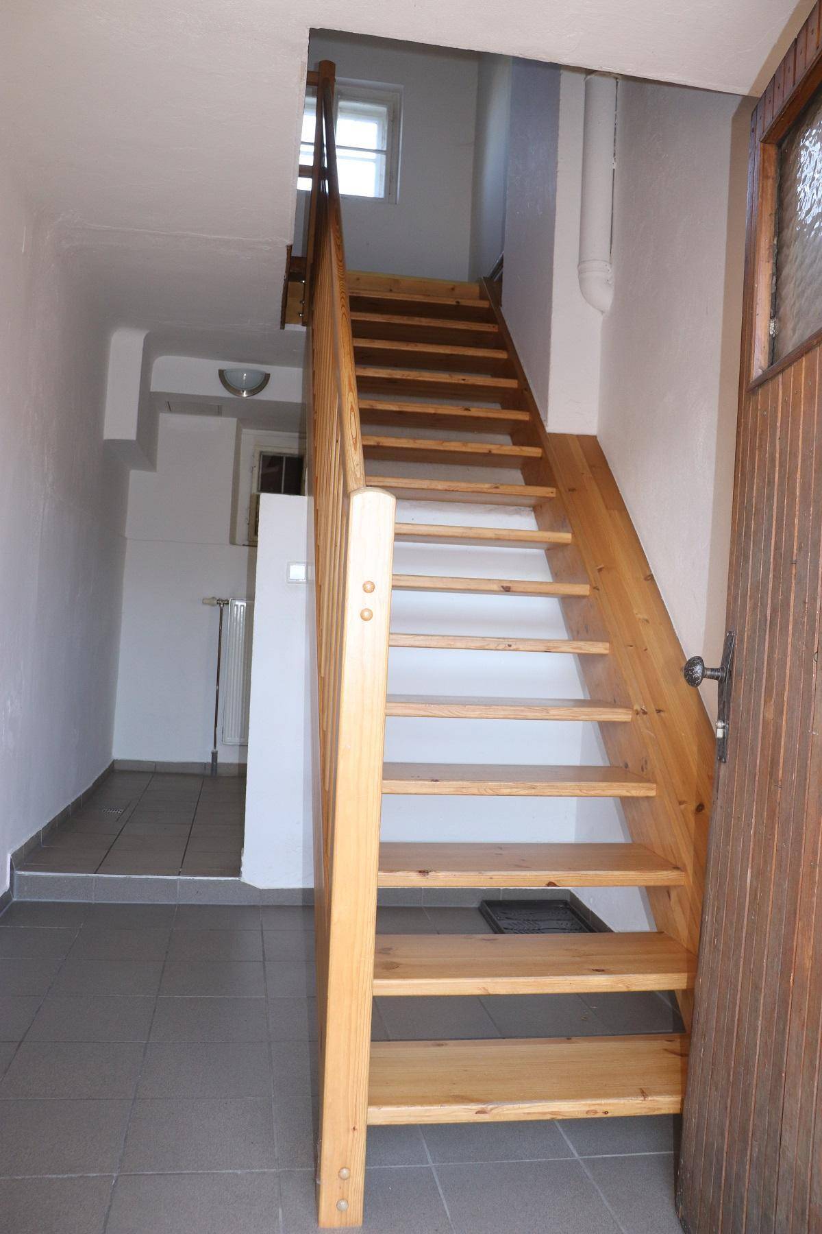 Robuste Holztreppe mit Geländer führt in ein oberes Stockwerk, der Boden ist gefliest.