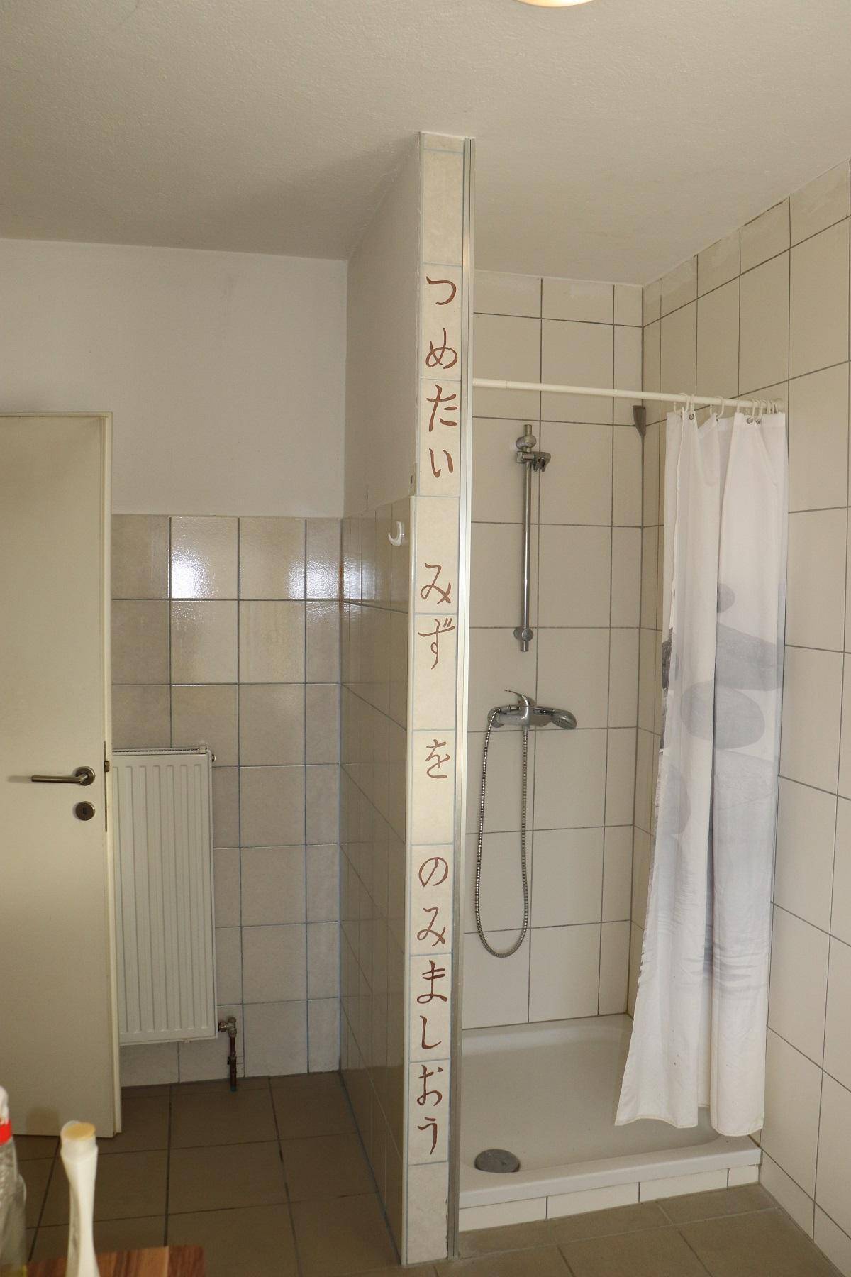 Badezimmer mit gefliester Dusche und Duschvorhang, ergänzt durch japanische Wandbeschriftung.