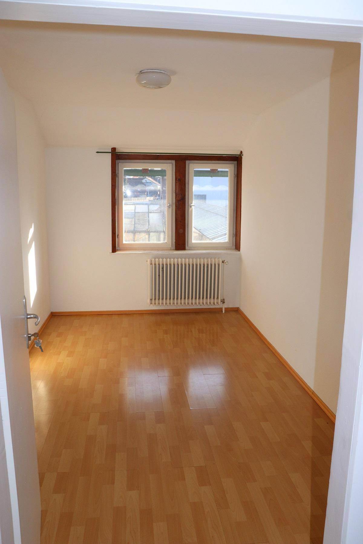 Freundliches Zimmer mit Laminatboden, zwei Fenstern und viel Tageslicht, von der Tür aus gesehen.