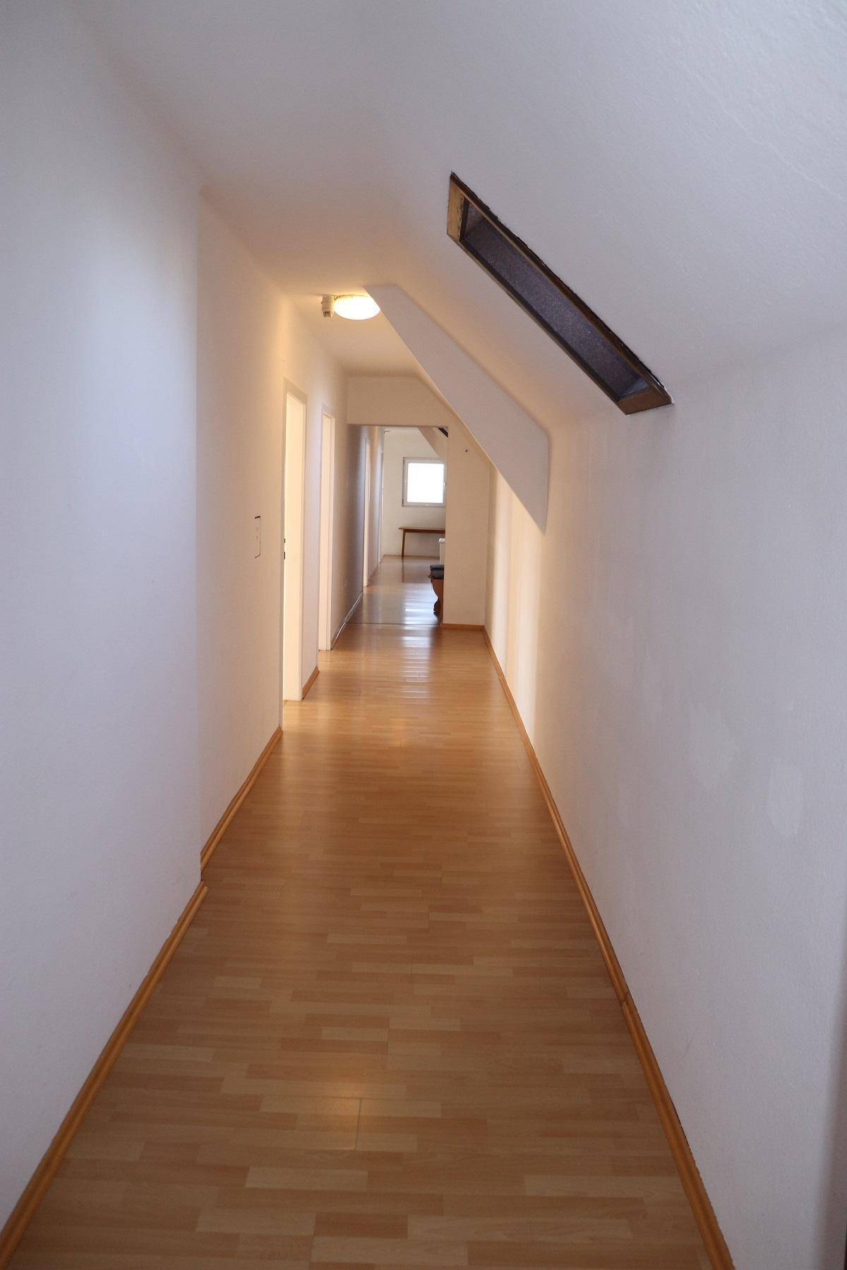 Langer, heller Flur mit Laminatboden und Dachschräge im oberen Bereich, der zu weiteren Räumen führt.