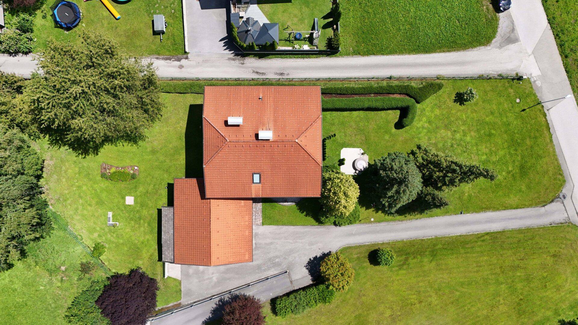 Übersichtliche Luftaufnahme des Hauses mit rotem Dach, umgeben von Gärten und Wegen.