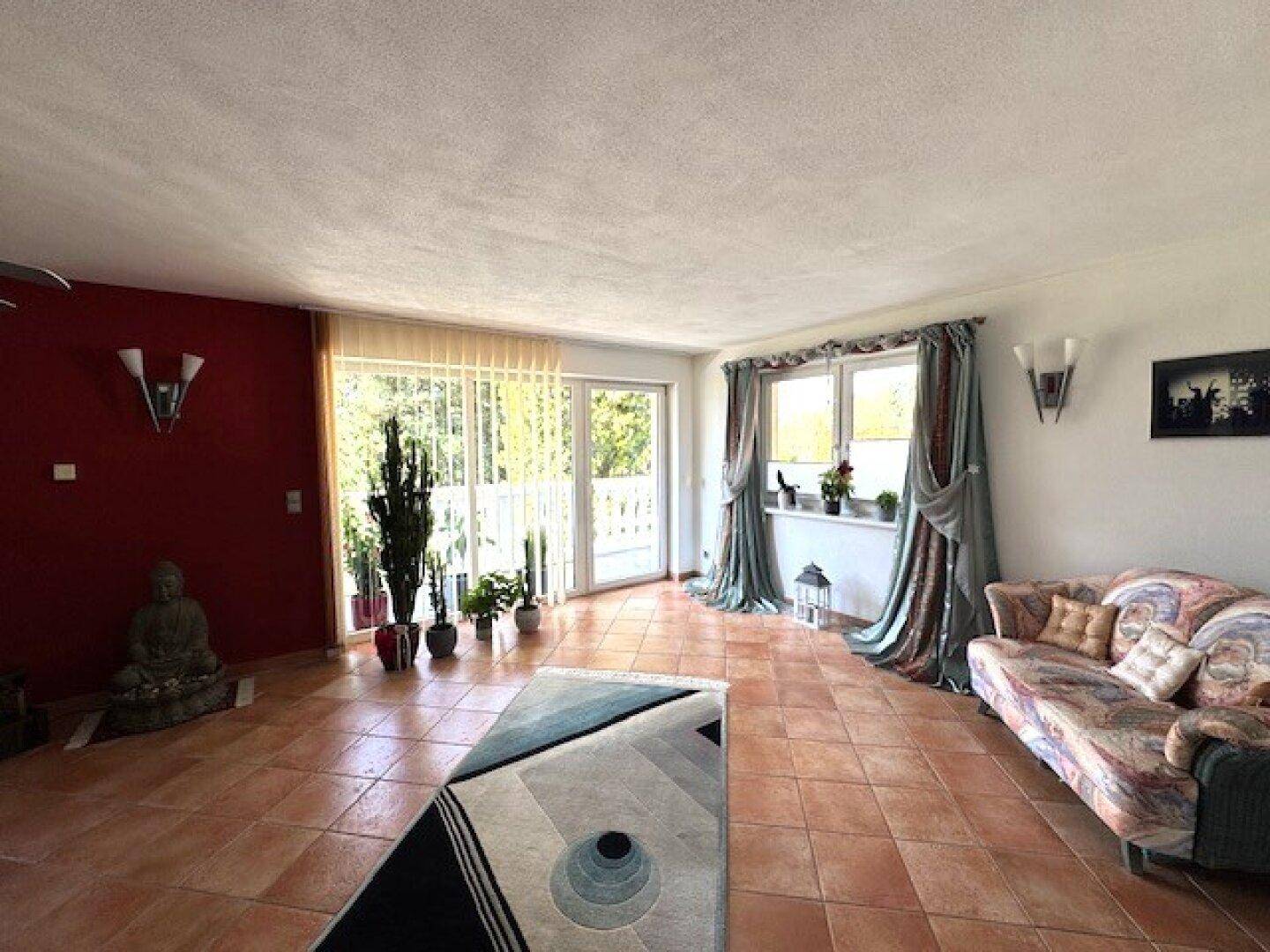 Wohnzimmer mit Terracottaboden, roter Akzentwand, Sofa und Balkonzugang.